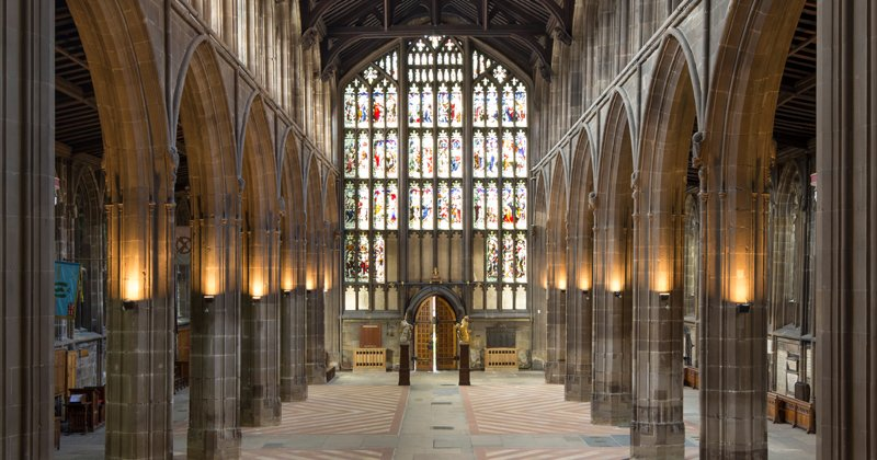 Interior of a historic church or cathedral with stone arches, stained glass windows, and wooden seating.