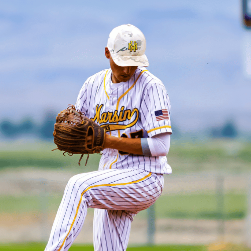 A young baseball player in a white pinstripe uniform with yellow accents, wearing a cap and glove, practicing on the field.