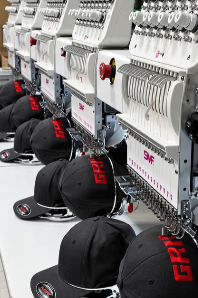 Industrial embroidery machines sewing black caps with red and white logos.
