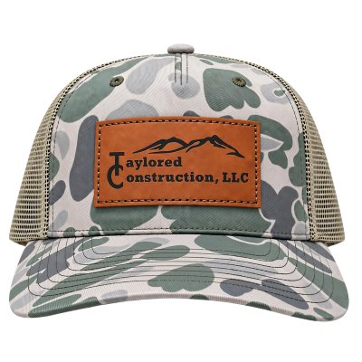 Camouflage baseball cap with tan leather patch reading 'Taylored Construction LLC' and a mountain logo.