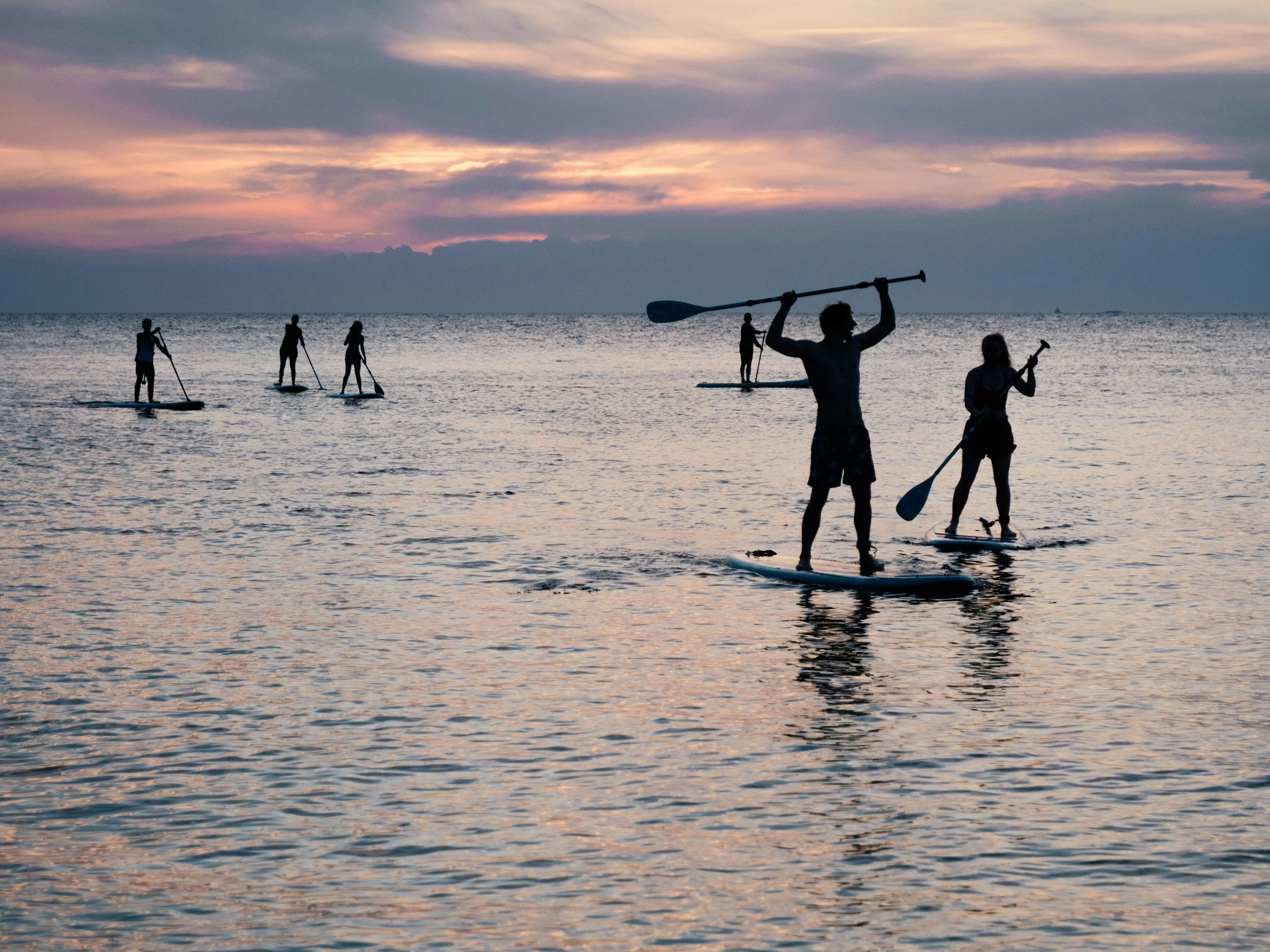 Group of people paddleboarding on calm water at sunset with a cloudy sky.