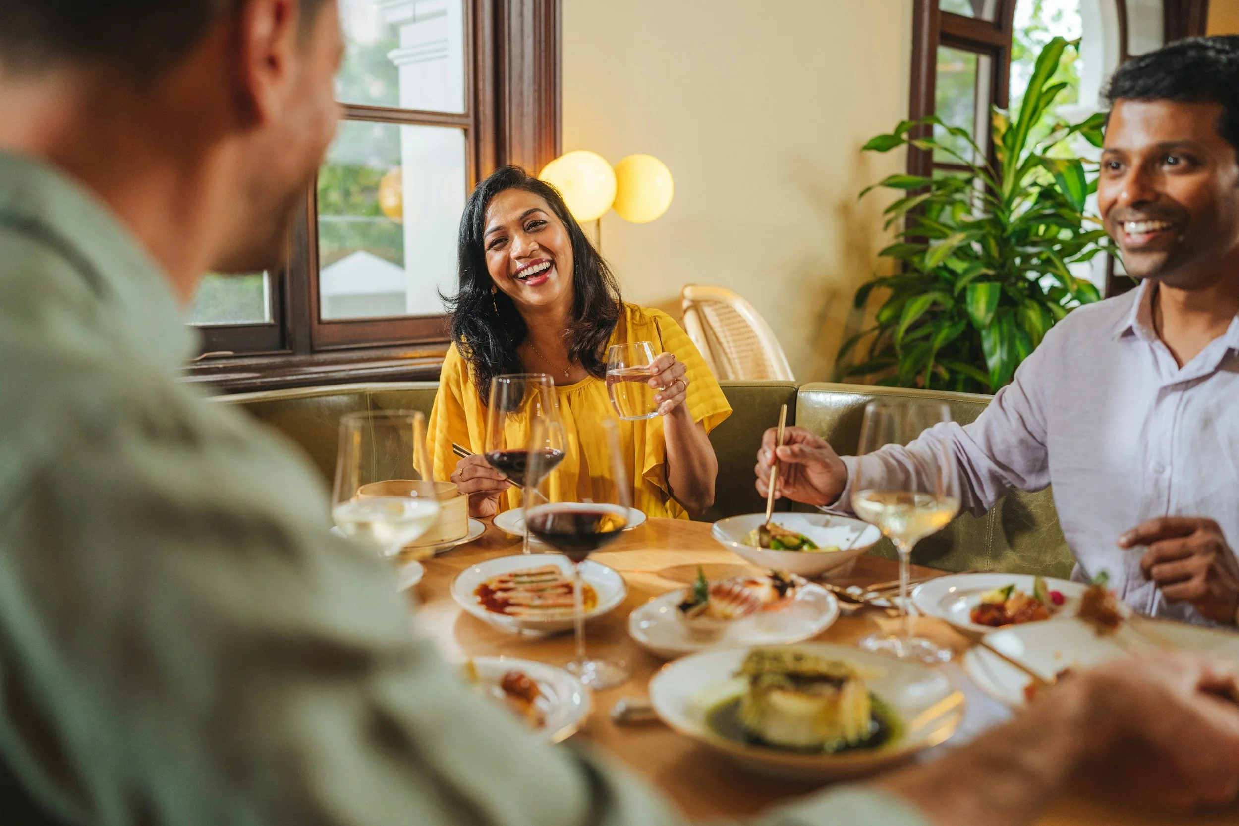 A group of people enjoying a meal together at a restaurant, with food and drinks on the table, smiling and engaging in conversation.