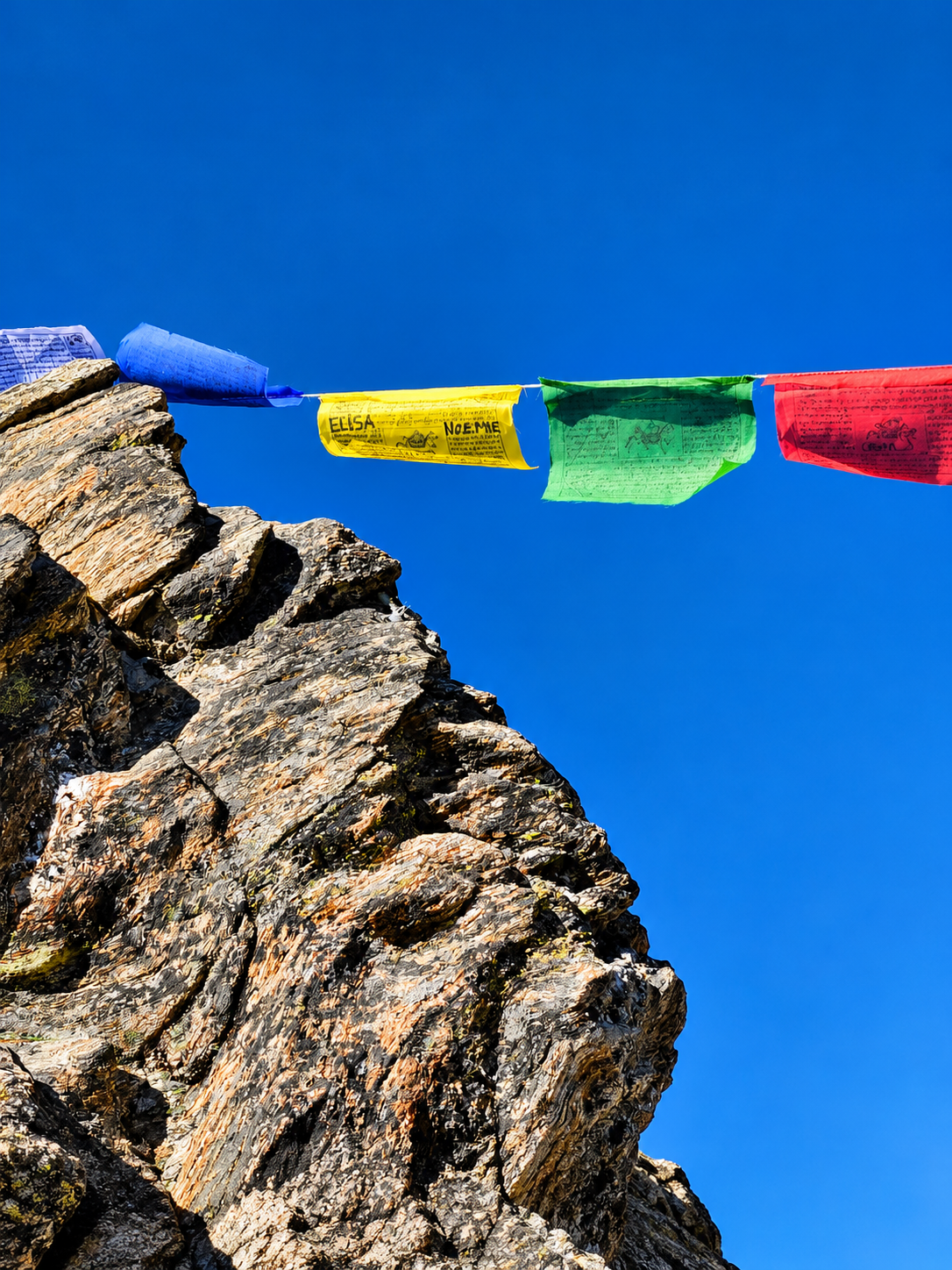 Bandiere di preghiera tibetane multicolori appese sopra una vetta rocciosa contro il cielo blu.