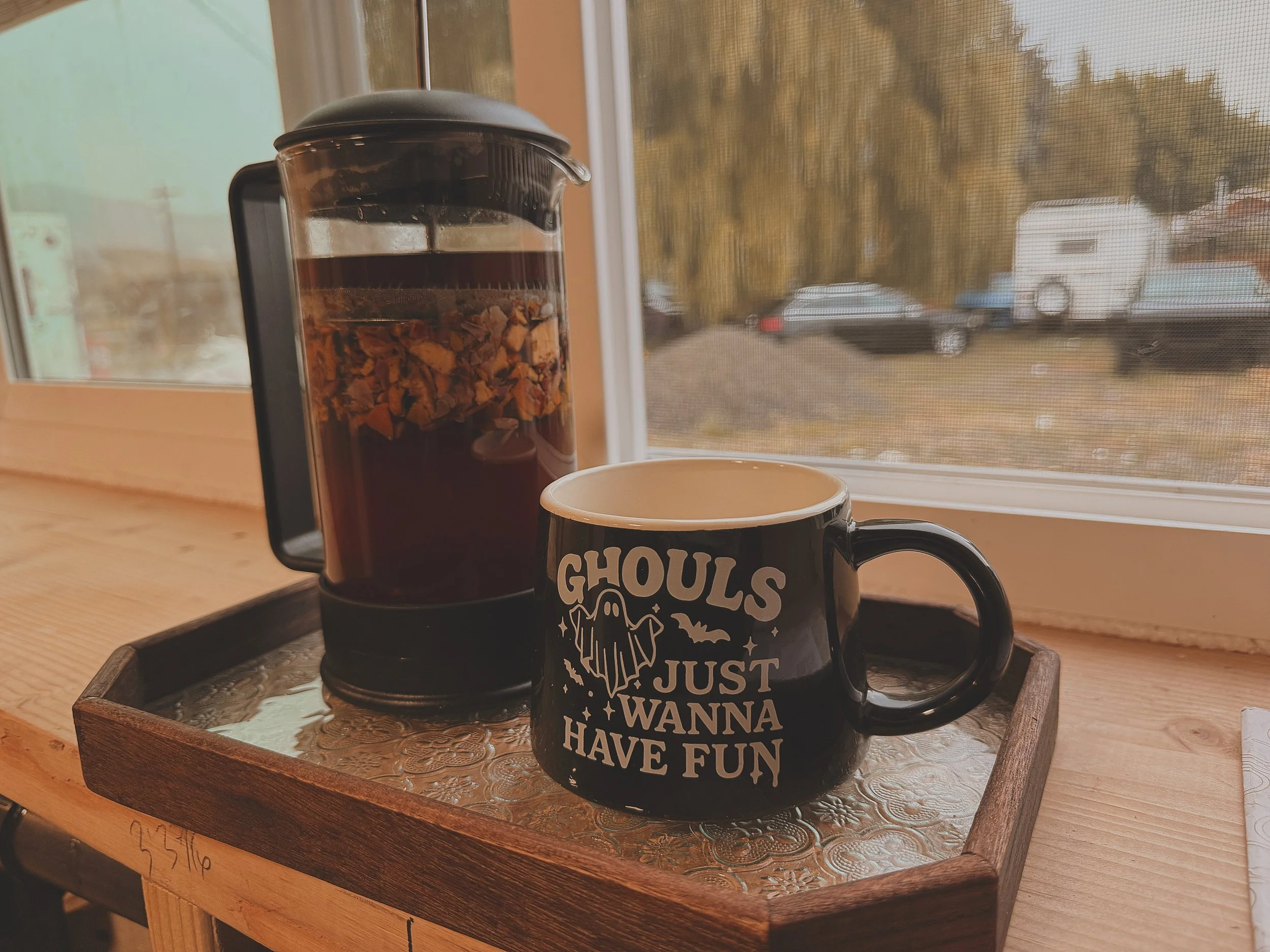 French press and black coffee mug on a wooden tray by a window