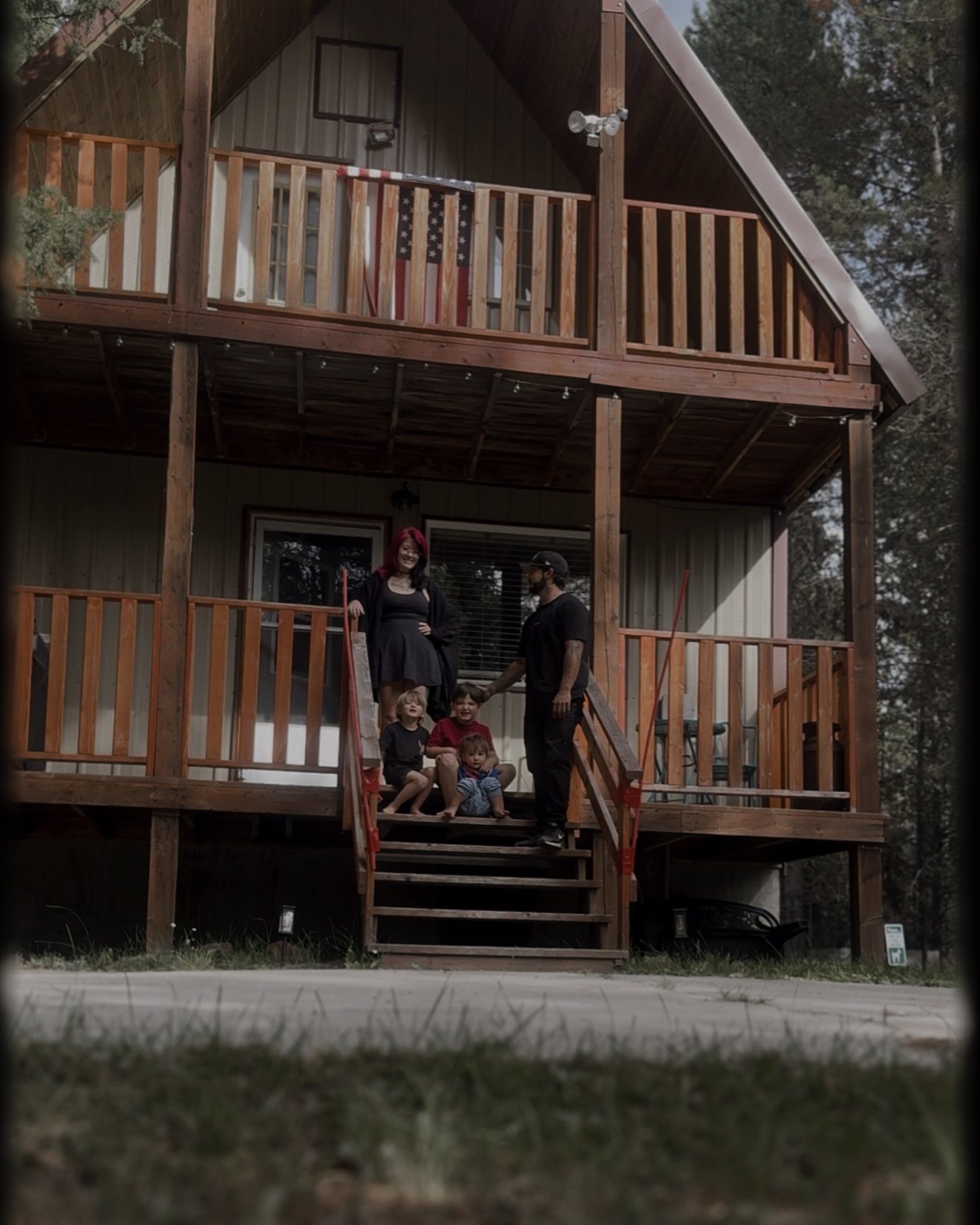 Family posing on the stairs and balconies of a rustic two-story cabin in the woods