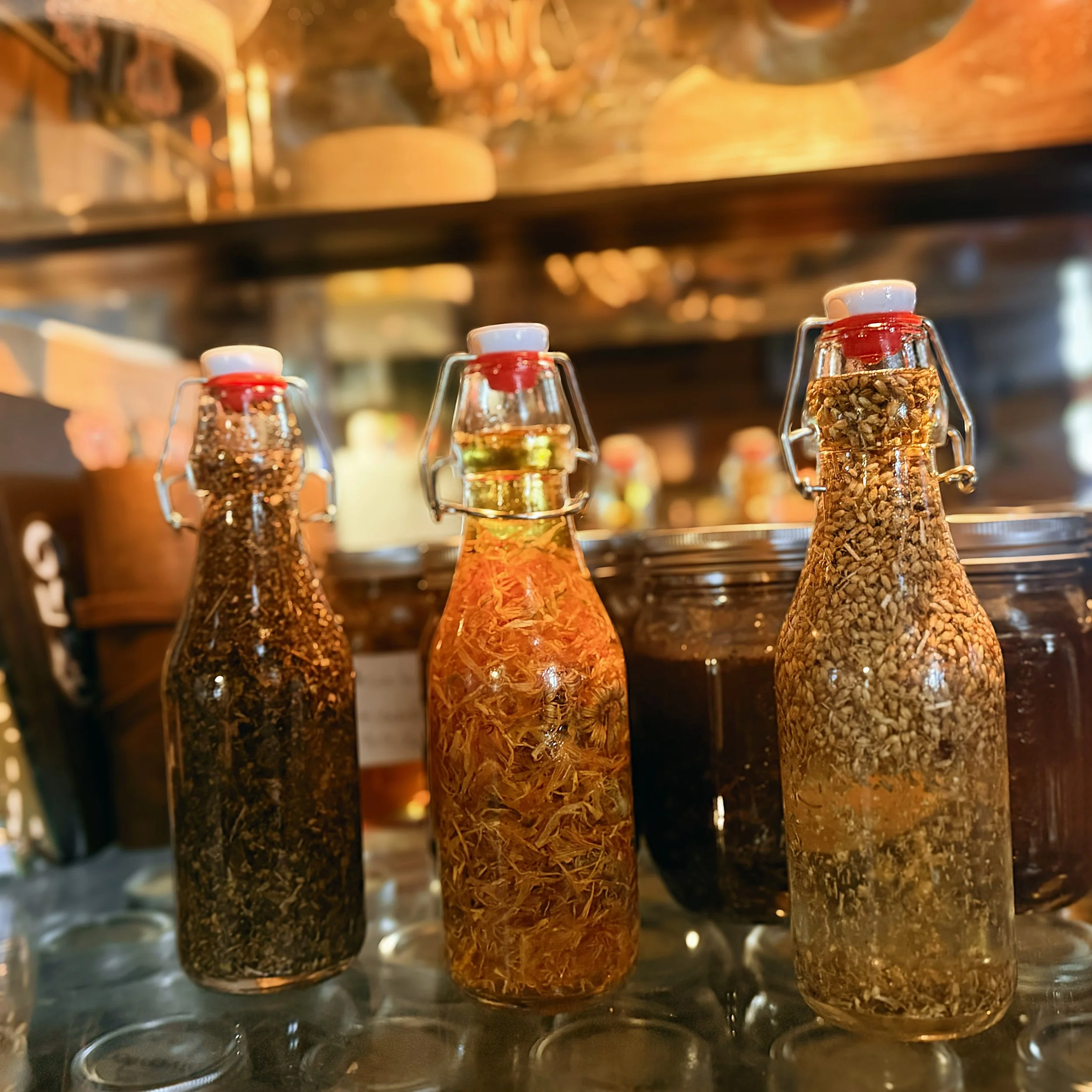 Three glass bottles filled with colorful dried herbs and spices on a warmly lit market counter