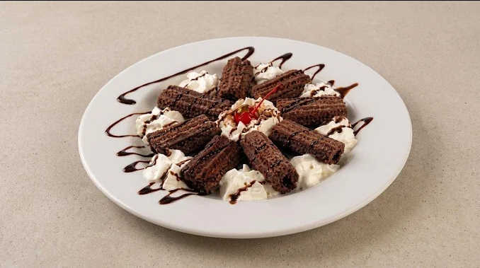 Chocolate wafer cookies with whipped cream and chocolate drizzle on a white plate garnished with a cherry.