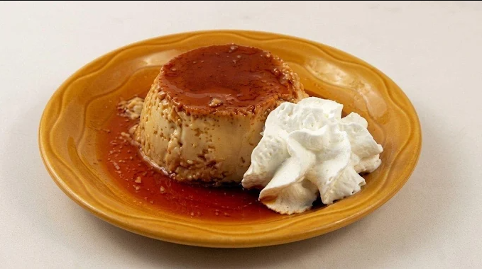 Caramel flan served with whipped cream on a yellow plate.