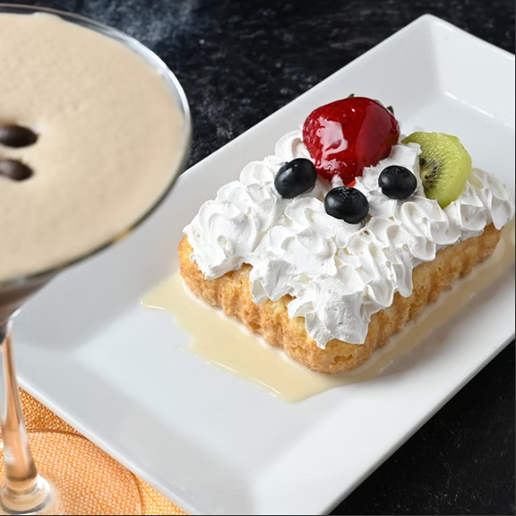 Dessert with whipped cream, fresh strawberries, blueberries, and kiwi on a rectangular white plate