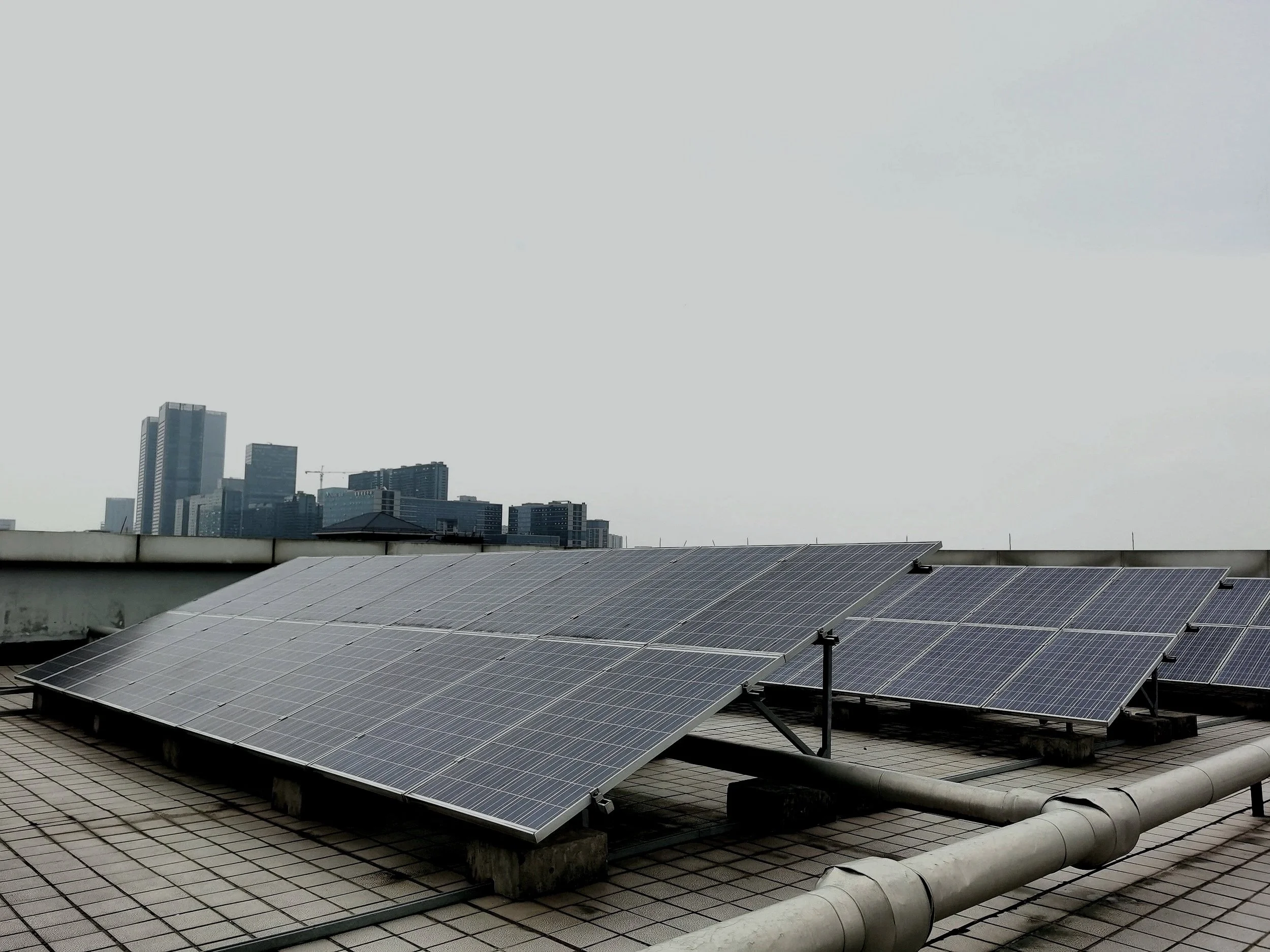 Solar panels installed on a flat rooftop with city buildings in the background and an overcast sky.