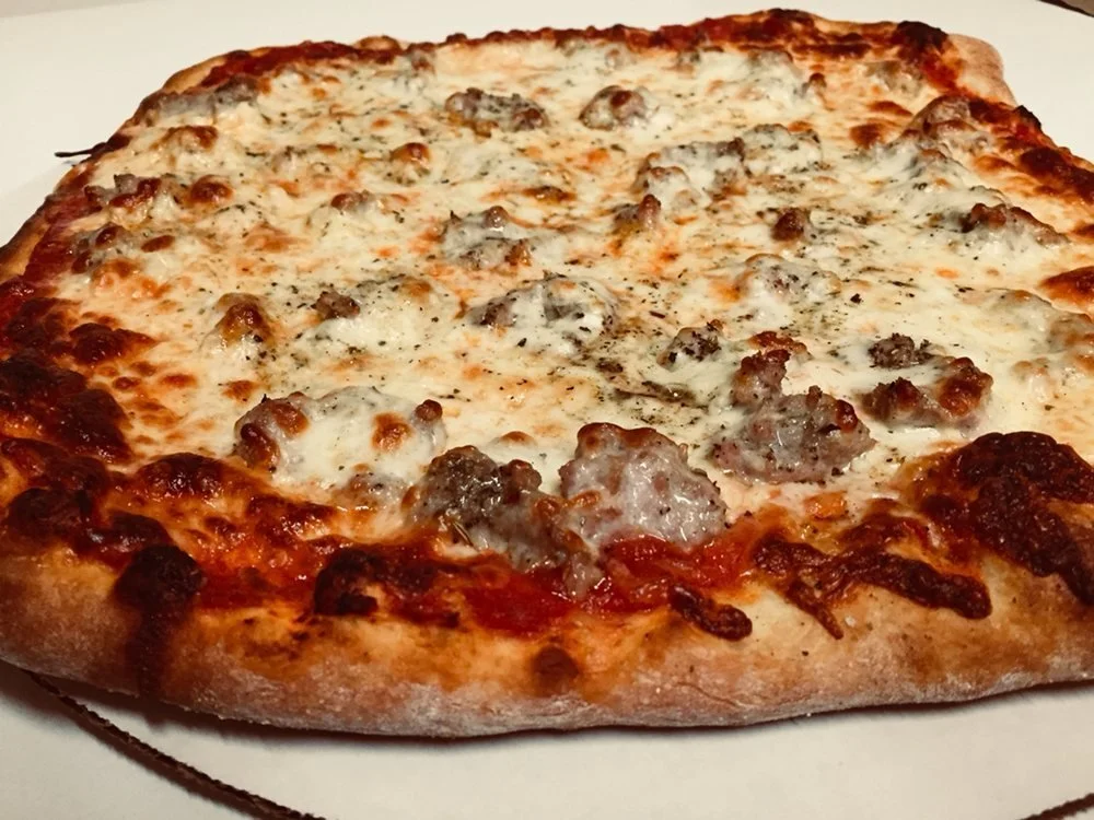A cheese pizza with sausage toppings on a white surface.