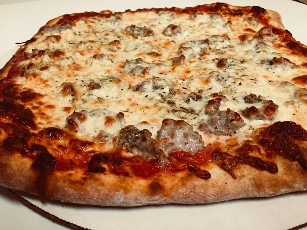 A close-up of a cheese and sausage pizza on a white plate.