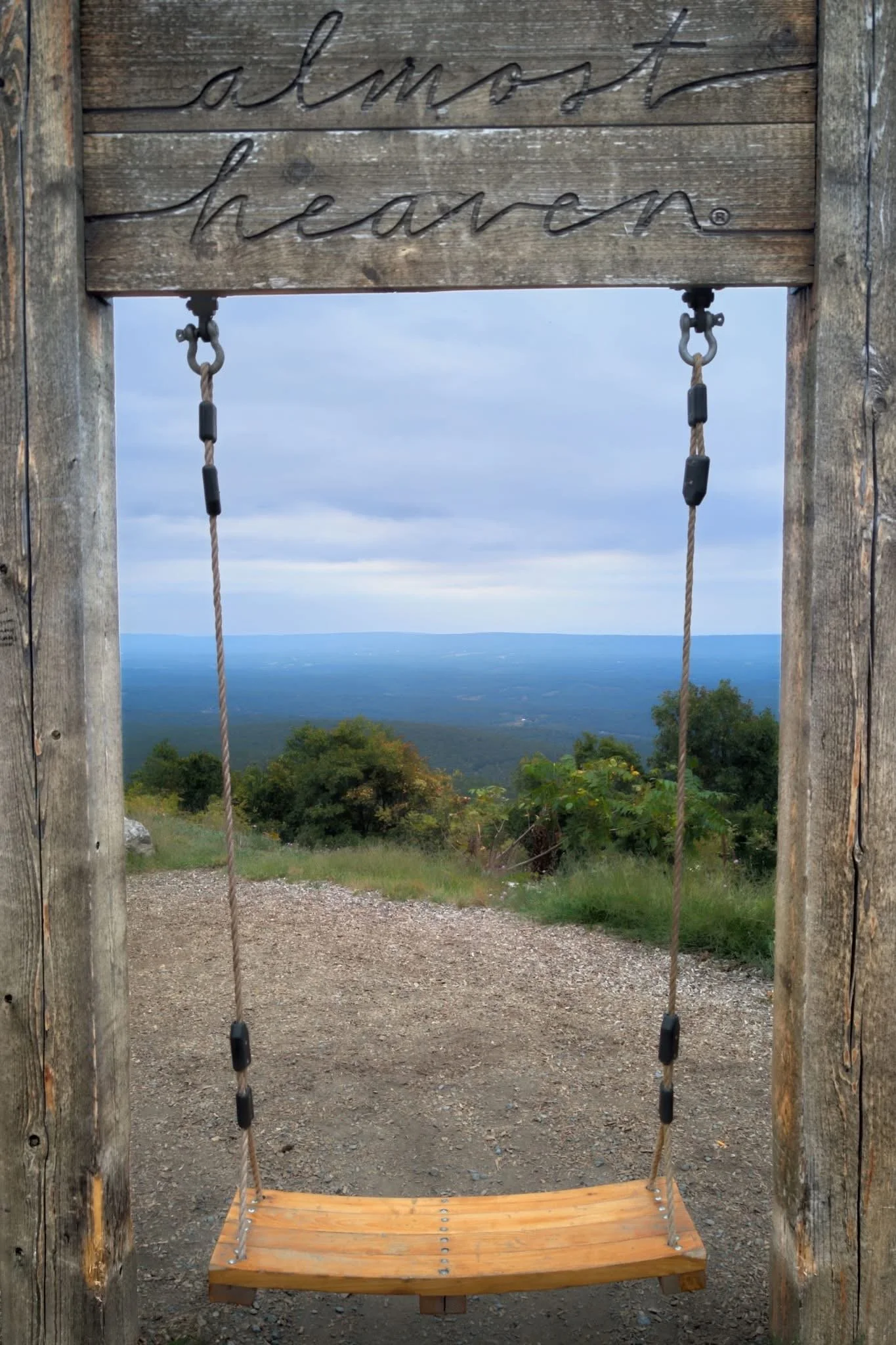  #1 Wooden swing set with cable swing attached, overlooking a scenic view of trees and mountains in the distance under a partly cloudy sky.