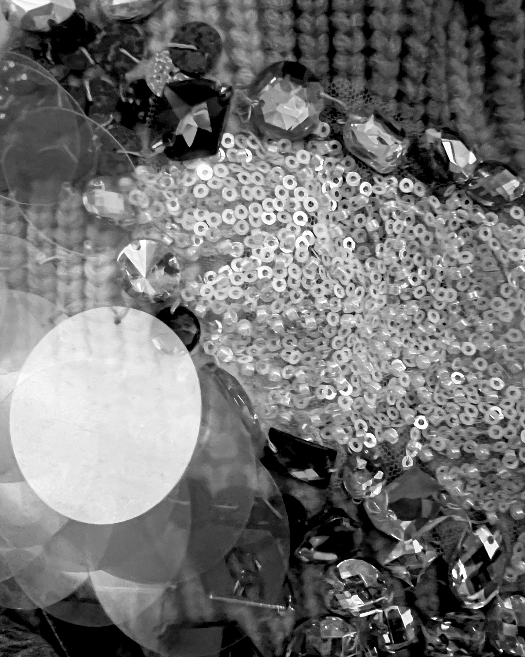 Close-up of various shiny, faceted gemstones and sequins scattered on a textured surface.