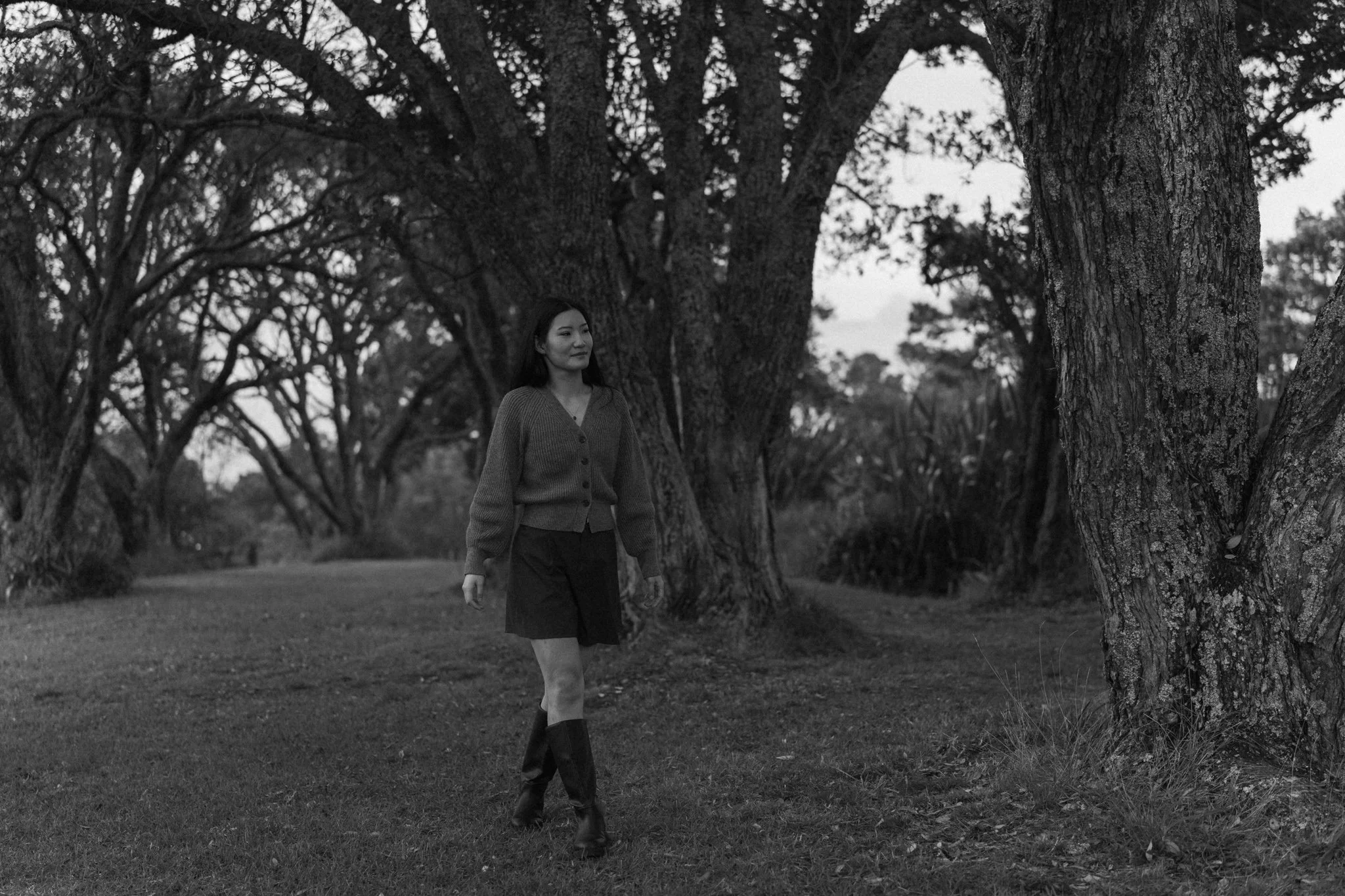 A woman walking through Musick Point, Auckland with large trees in the background, captured in black and white.