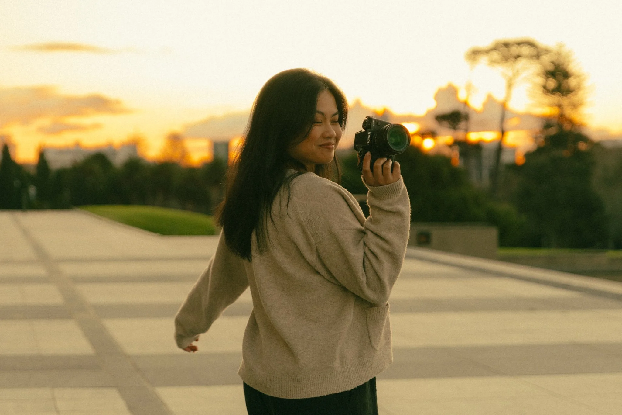 Jille holding a camera, standing outdoors during sunset in front of Auckland Museum. Branding image of an Auckland-based cinematic photographer.