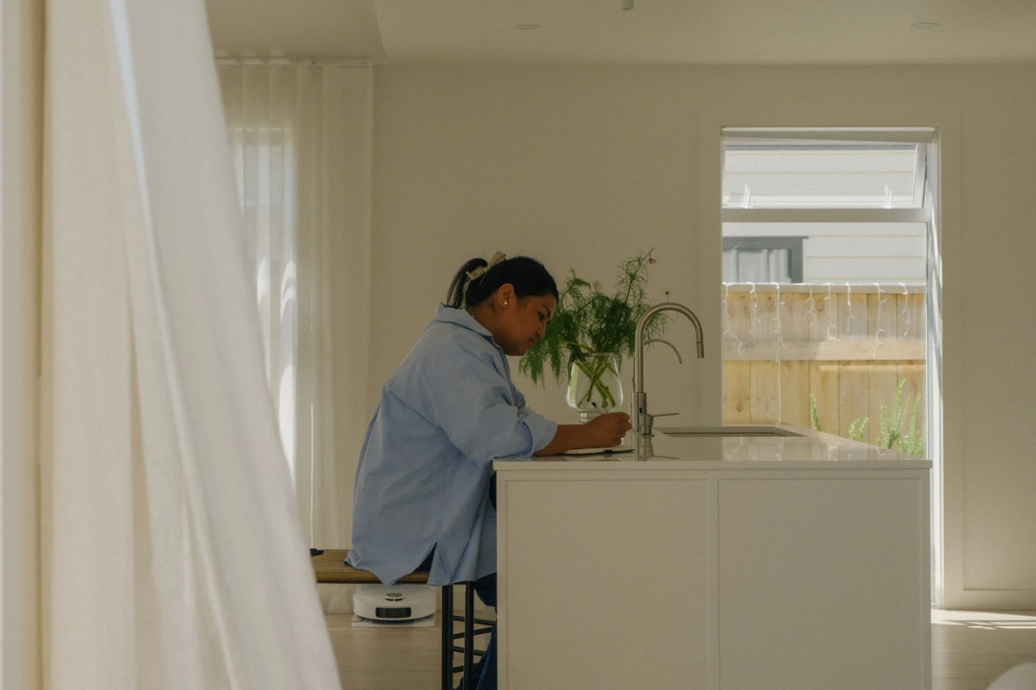 A female business owner sitting on a barstool by a kitchen island, writing in her notebook. Taken at Another White Casita, Wellington, New Zealand.
