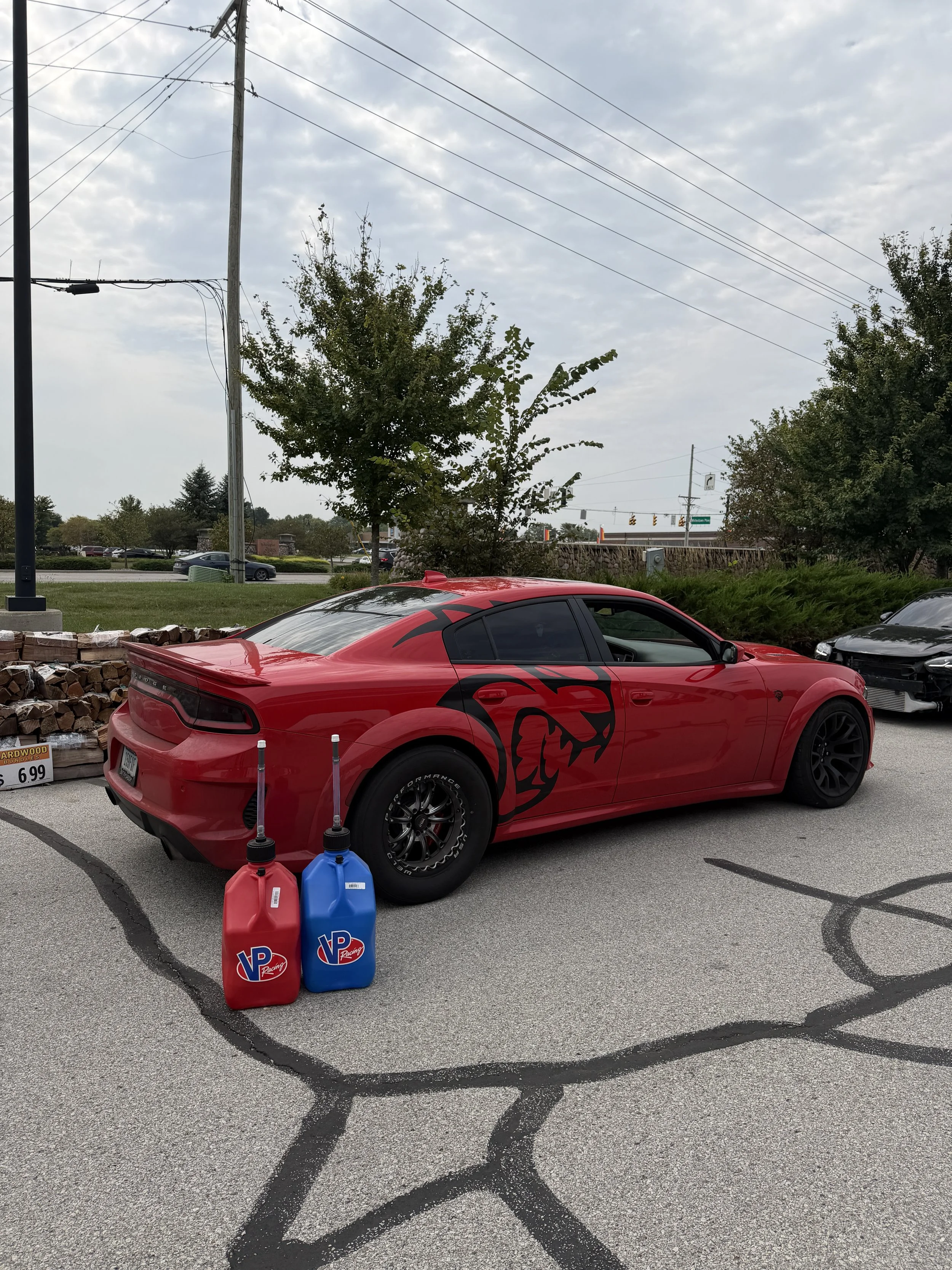 Red race car with black graphics parked in a parking lot with two VP racing fuel containers in front of it.