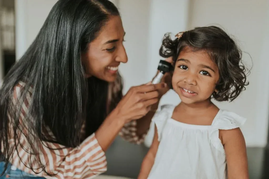 Dr. Shrinidi Mani examining a young girl's ear with a medical device.