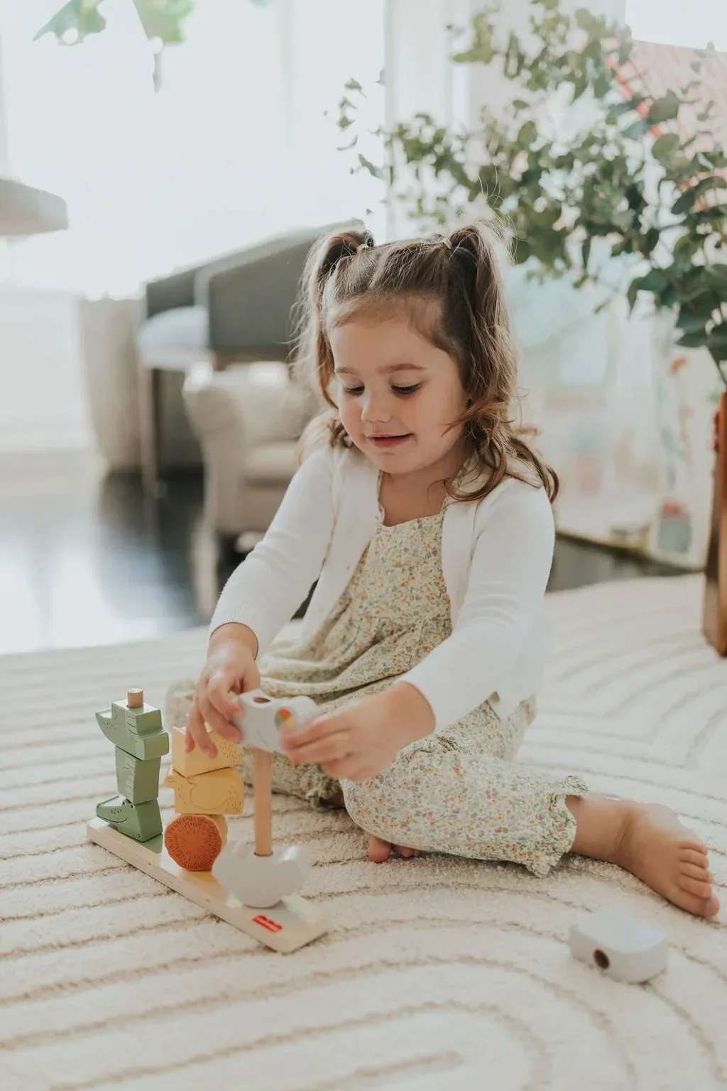 Young girl playing with a wooden toy train on a living room rug