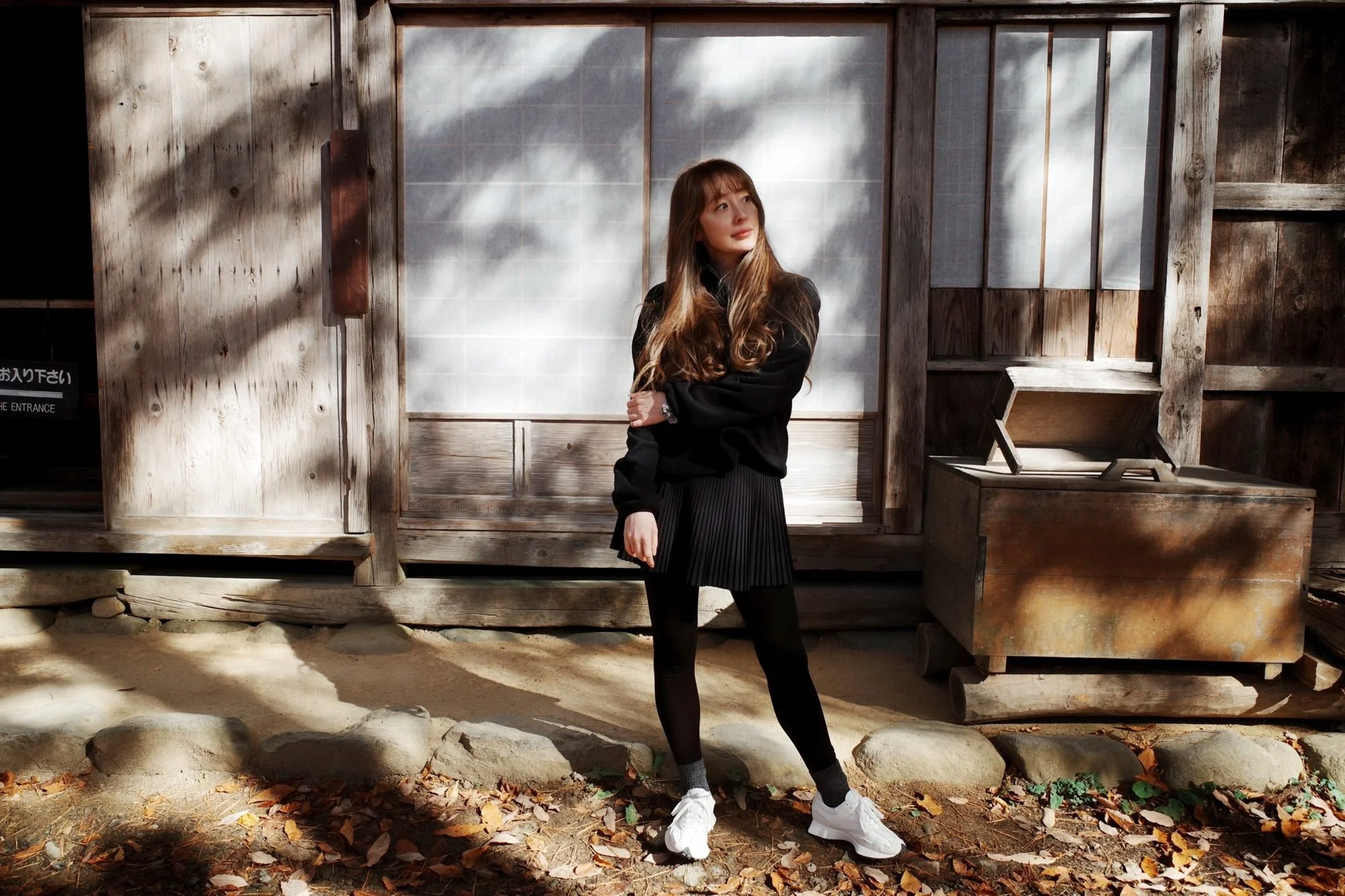 Kristen standing in dappled autumn light outside an old wooden house