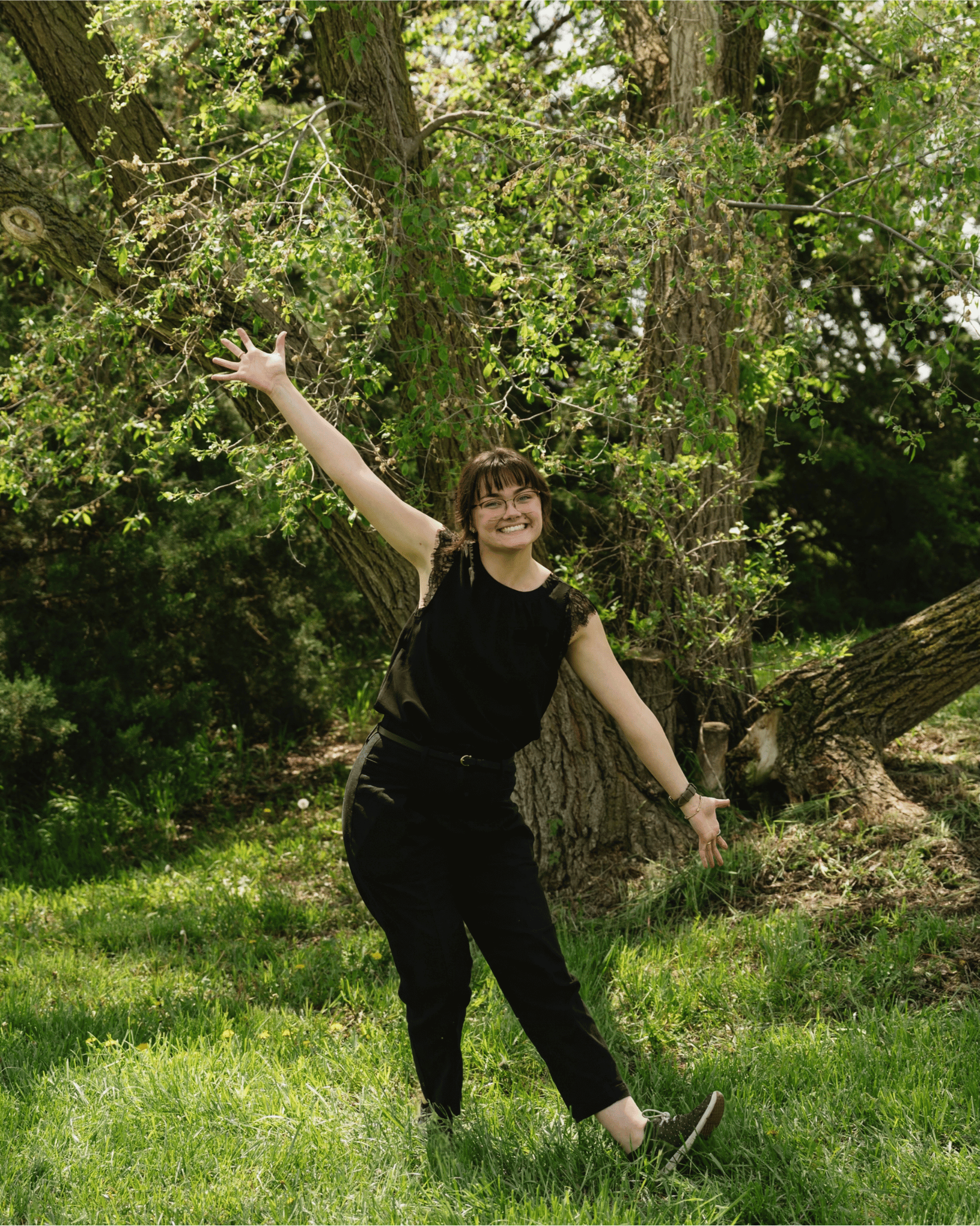 Grace Graham, owner of GG Floral Studio in a black top and pants standing outdoors in front of a large tree.