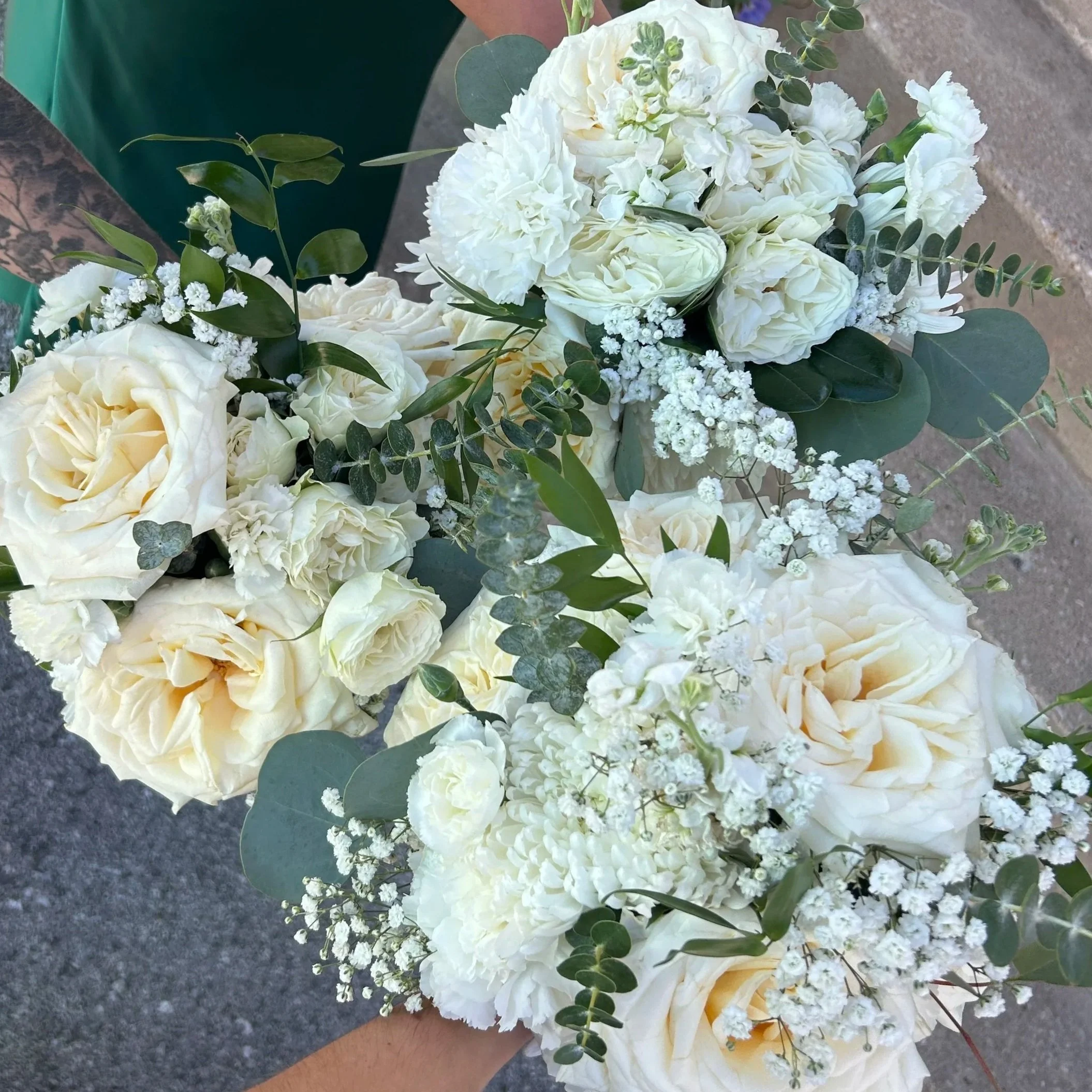 Three white and green bridesmaid bouquets with roses, baby's breath and carnations accented with ruscus and eucalyptus.