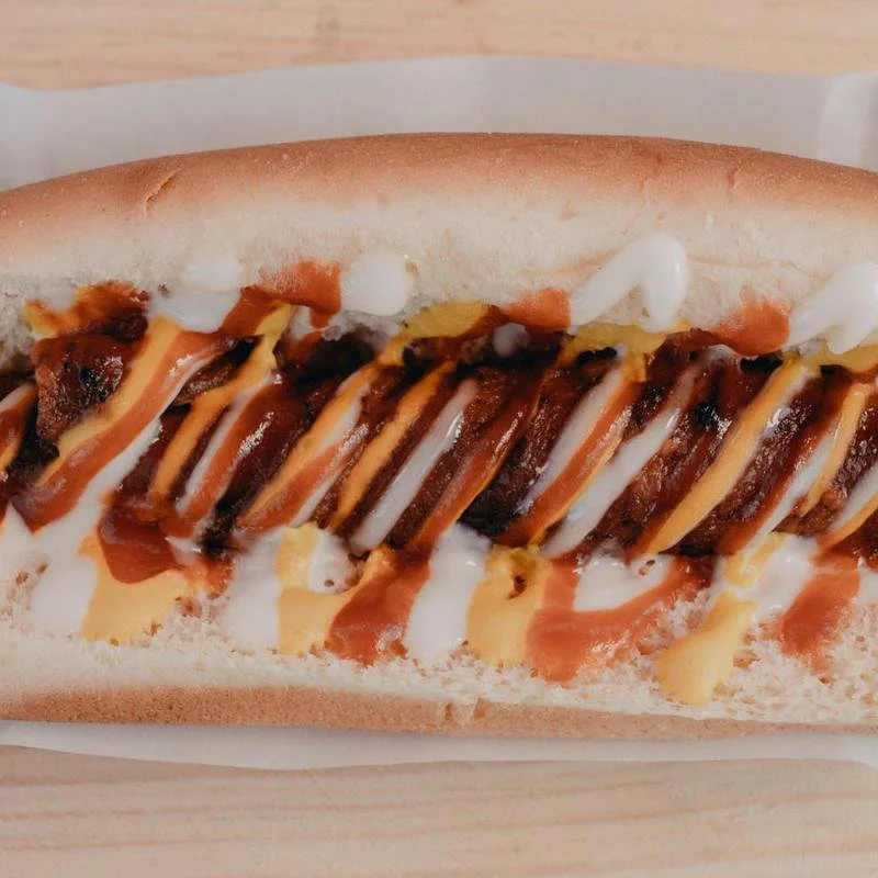 Close-up of a hot dog with mustard, ketchup, mayonnaise, and grilled onions in a bun.