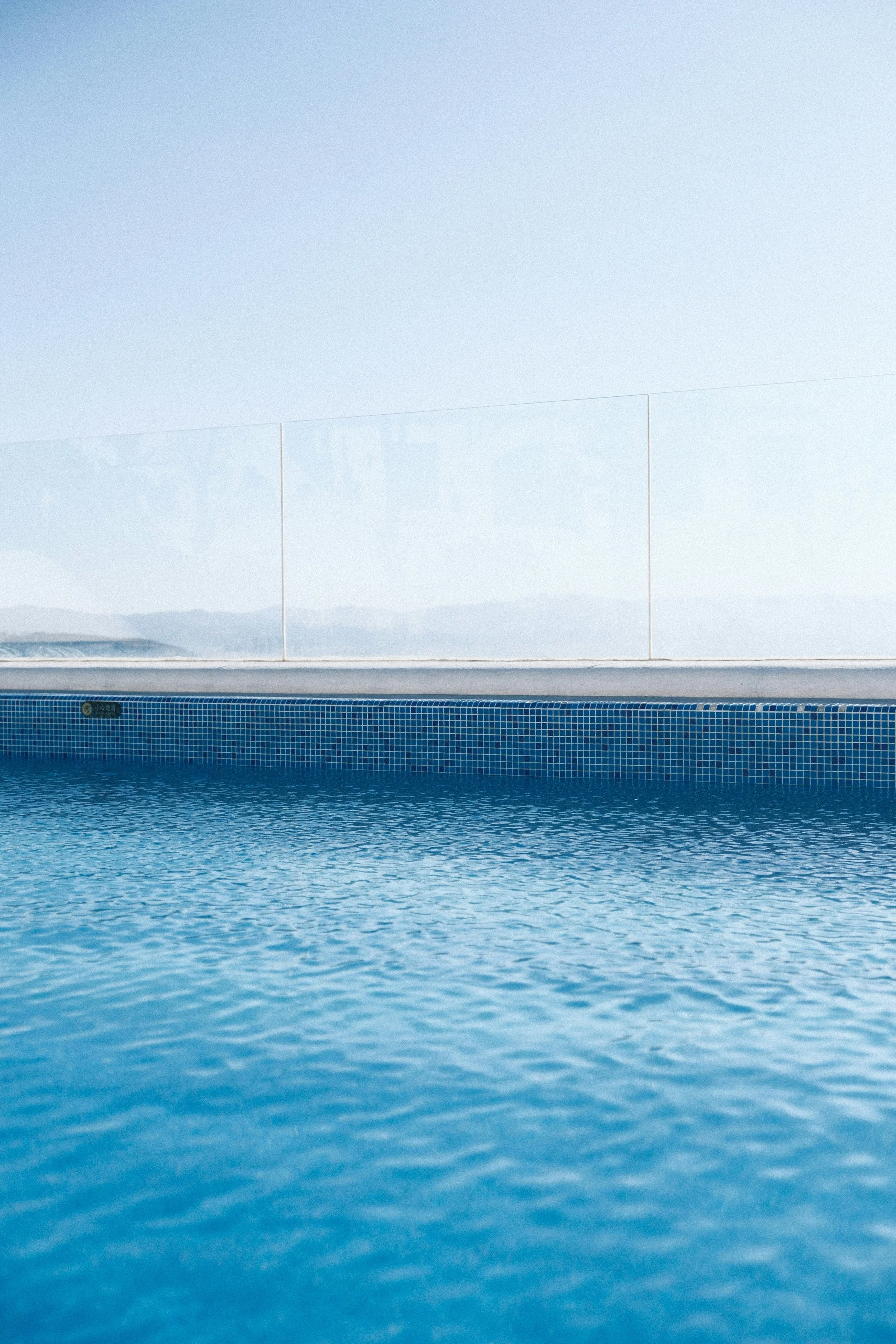 Vue d'une piscine avec un mur de verre transparent et un ciel clair en arrière-plan.