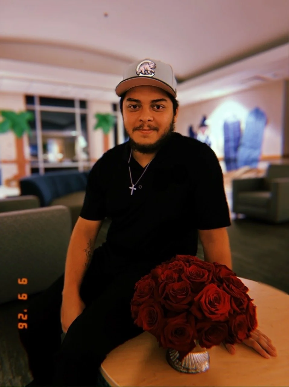 Young man seated indoors holding a bouquet of red roses.