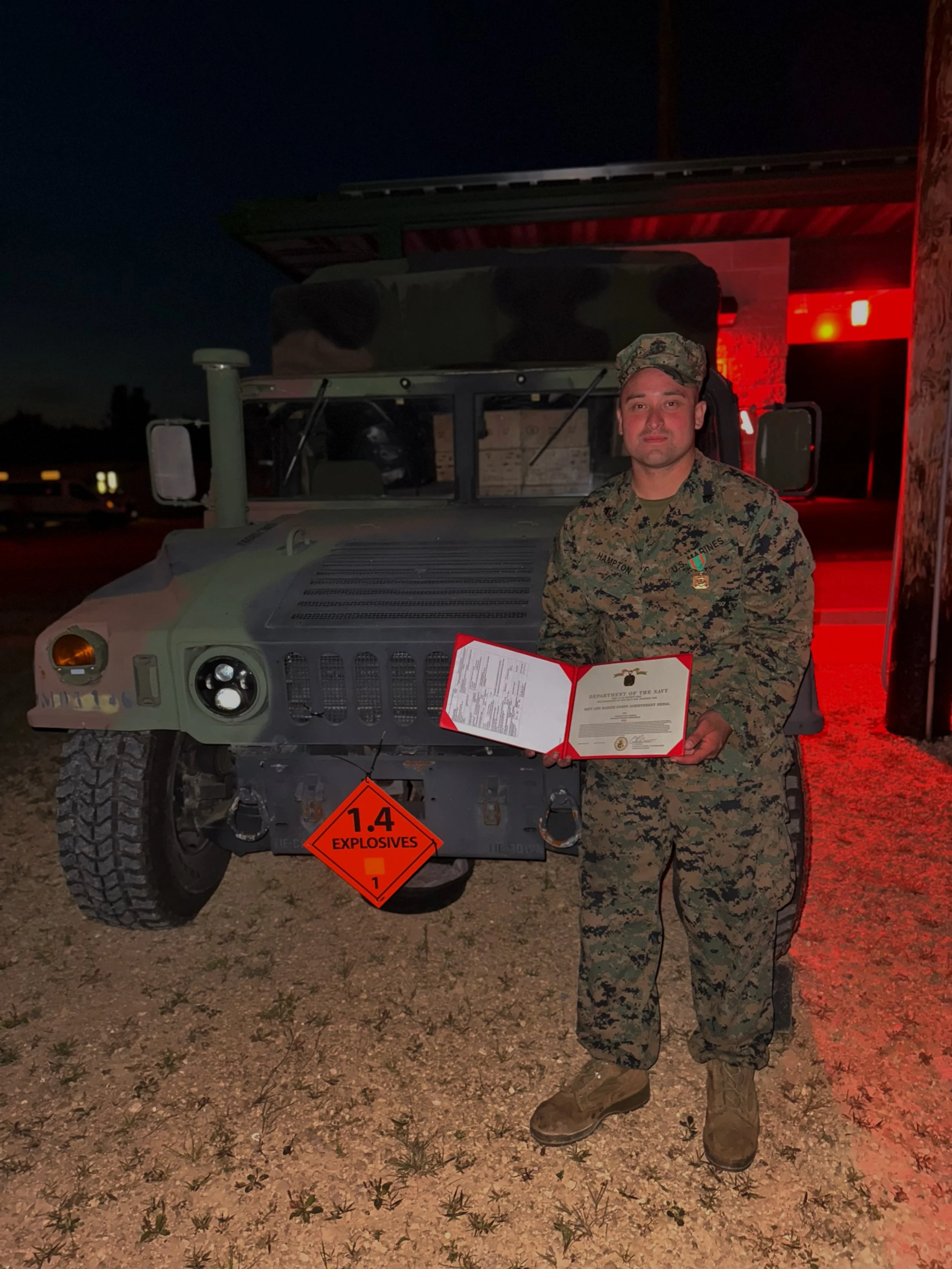 U.S. Army soldier in uniform standing in front of a military vehicle while holding a certificate.