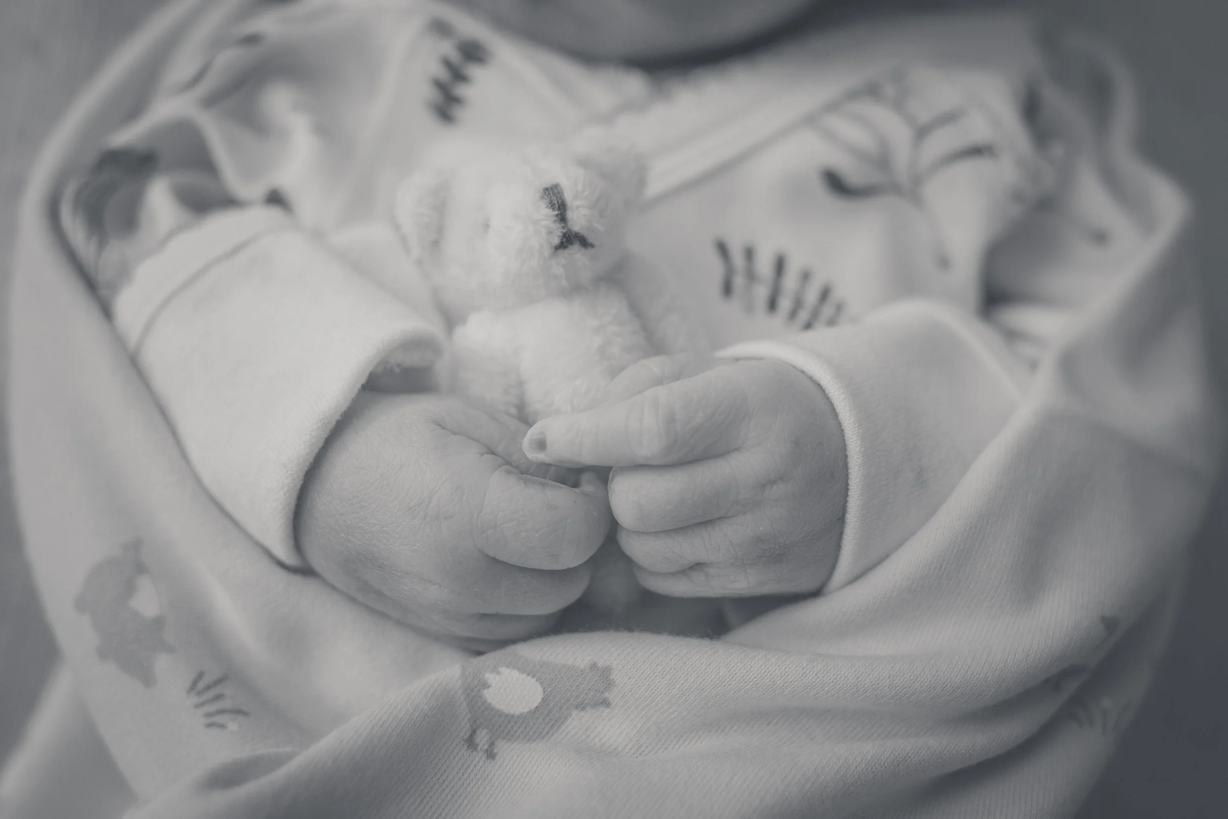 Close-up of a newborn baby being held gently in someone's hands, wrapped in a soft blanket, in black and white.