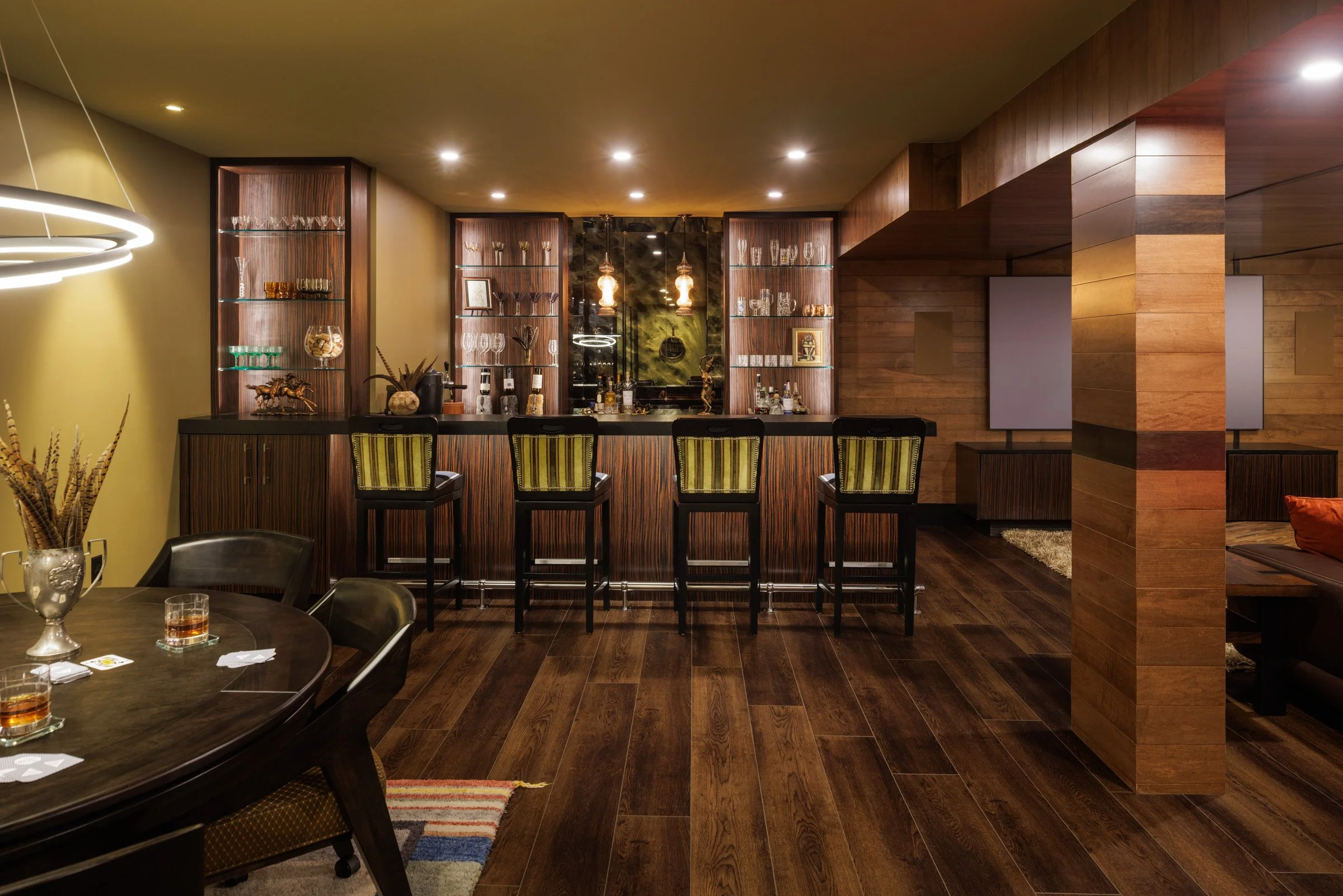 Home bar with rich wood cabinetry, glass-front shelves and upholstered bar stools