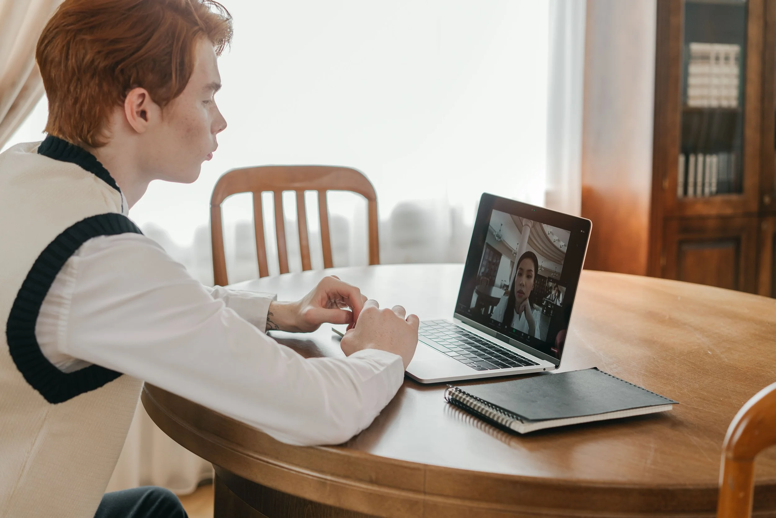 Ein junger Mann sitzt am Tisch vor seinem Laptop und ist in einem Videocall mit einer jungen Frau.