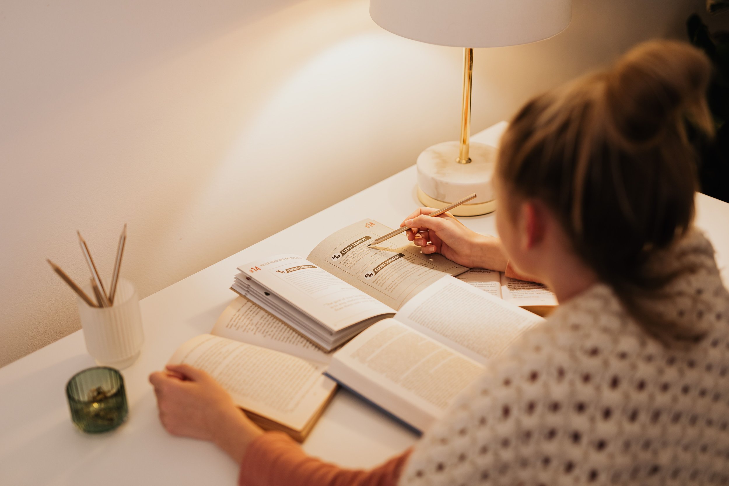 Eine Studentin sitzt allein am Tisch und lernt aus 3 aufgeschlagenen Büchern.
