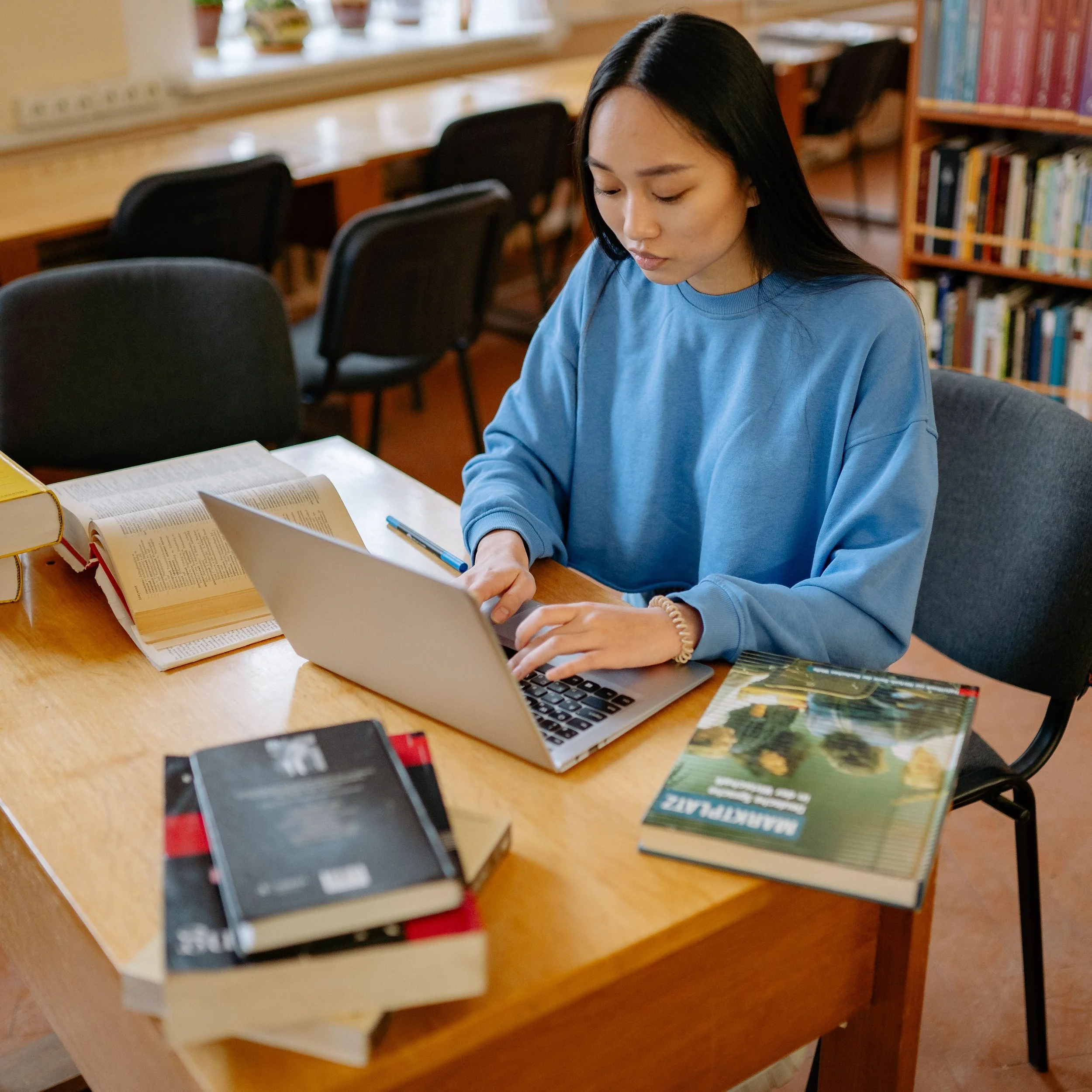 Junge Frau lernt Deutsch am Laptop online und viele Lernbücher liegen links und rechts von ihr.