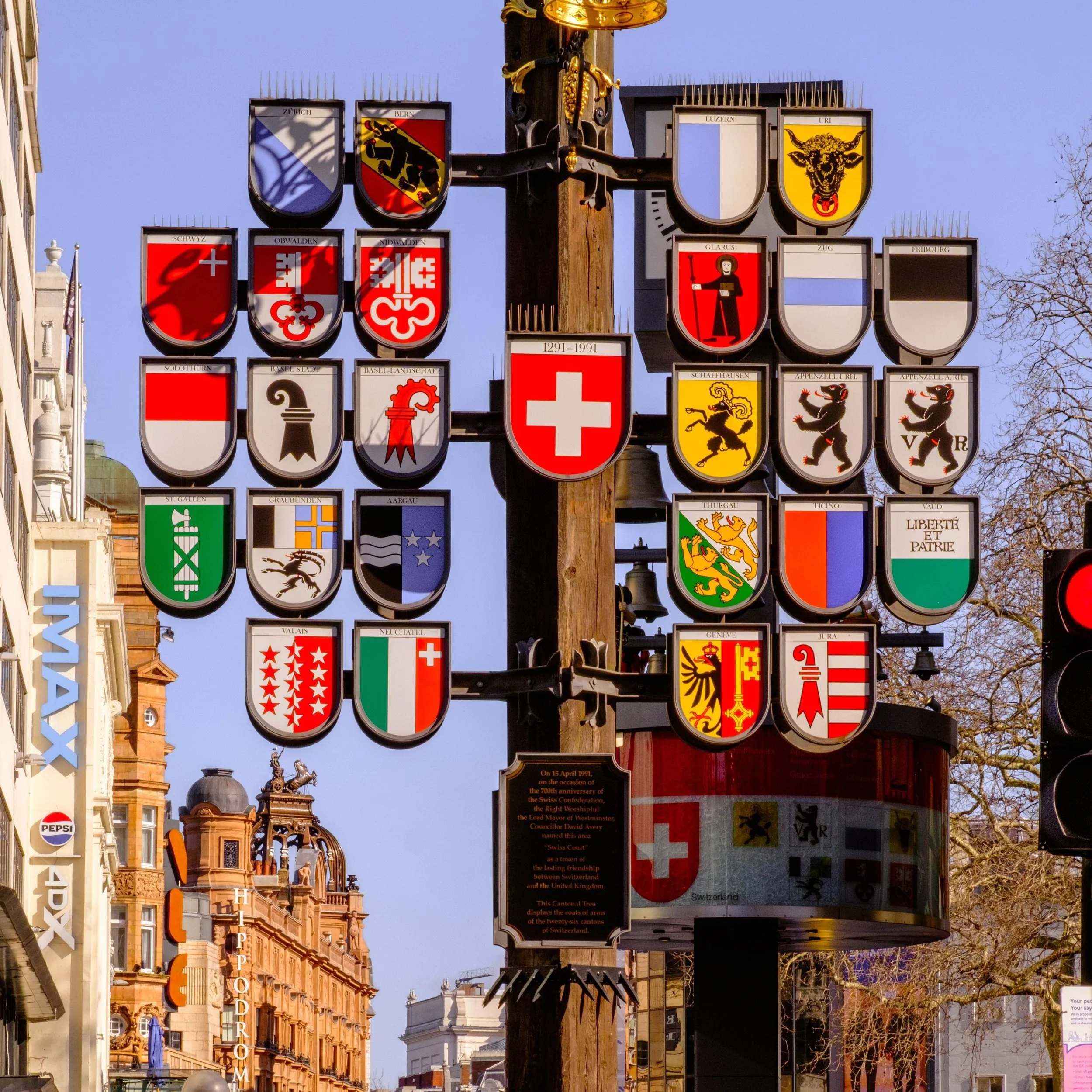 Ein Holzpfahl in einer Stadt, dekoriert mit allen Kantonswappen und in der Mitte das Schweizerwappen.