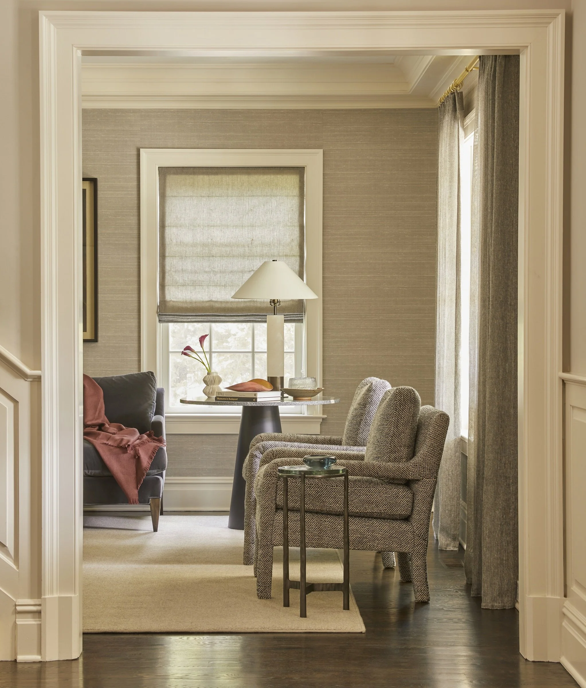 View through a doorway into a neutral bedroom with an upholstered chaise