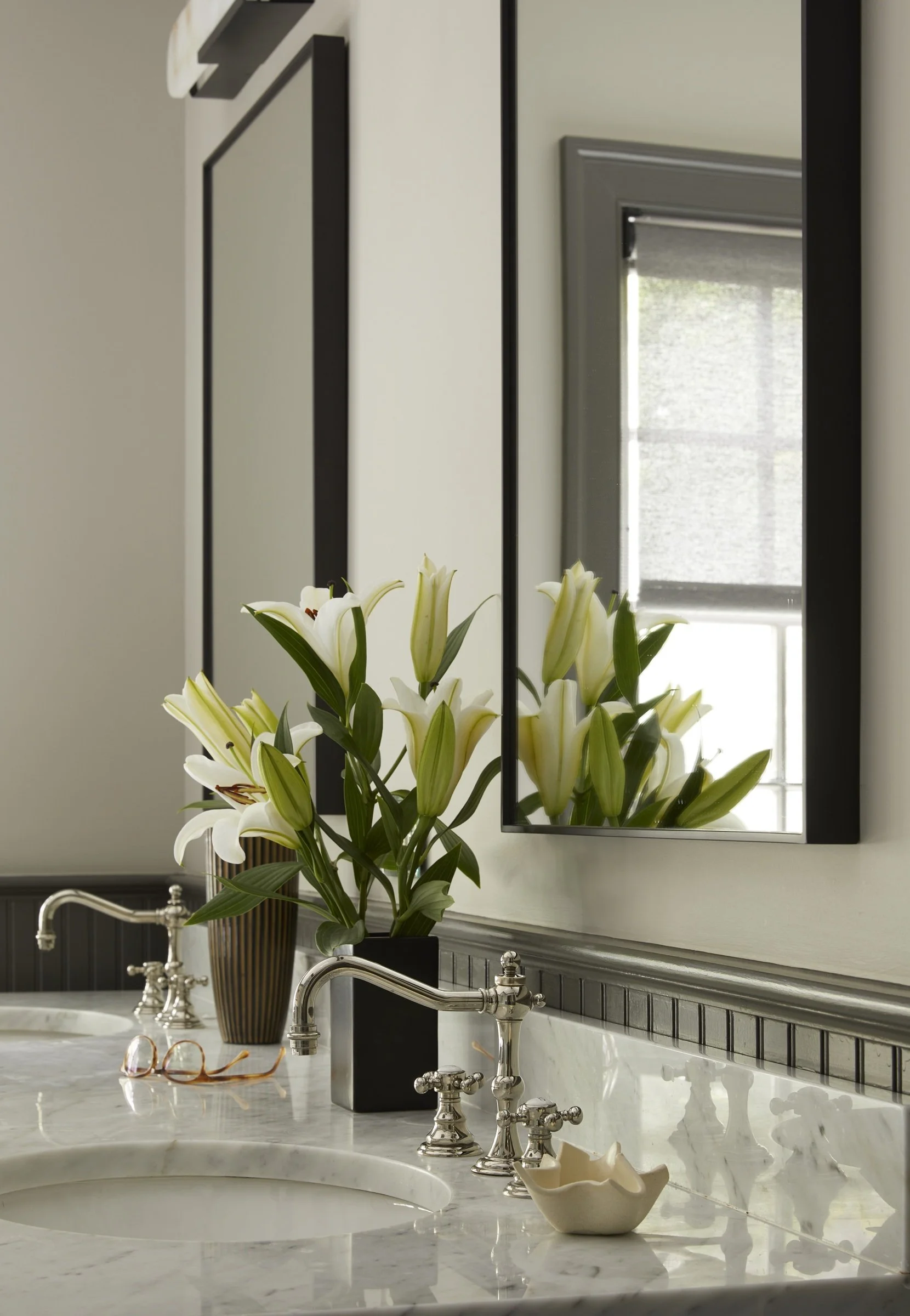 Bathroom vanity with a framed mirror and a vase of white flowers