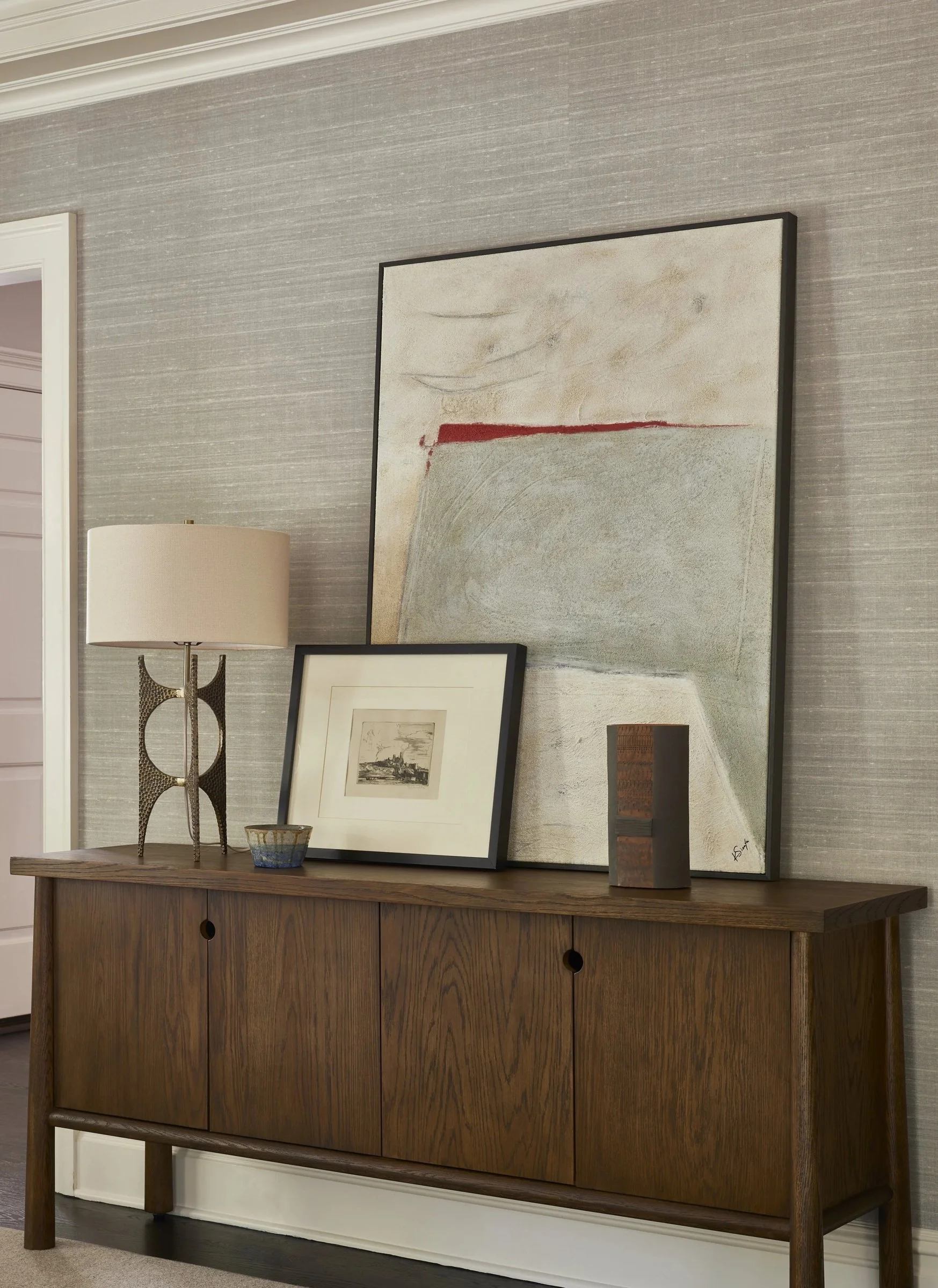 Wood cabinet with framed artwork and a table lamp