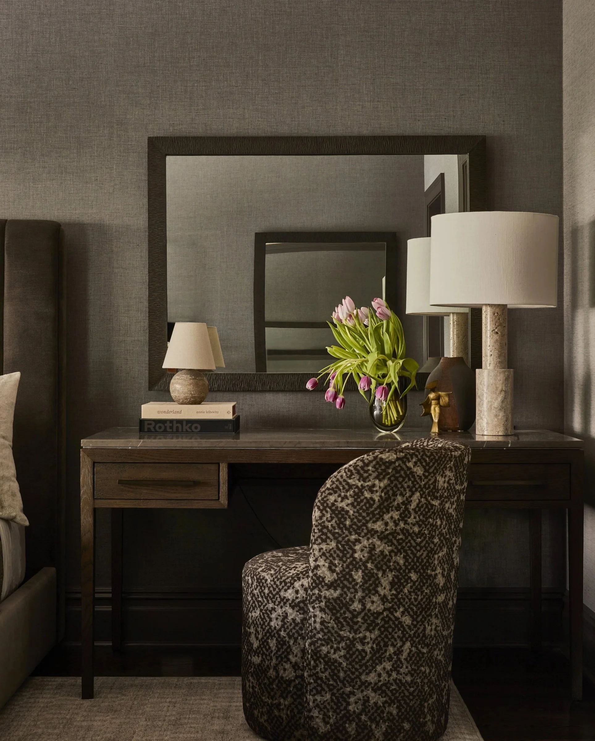 Wood desk and floral upholstered chair beneath a framed mirror