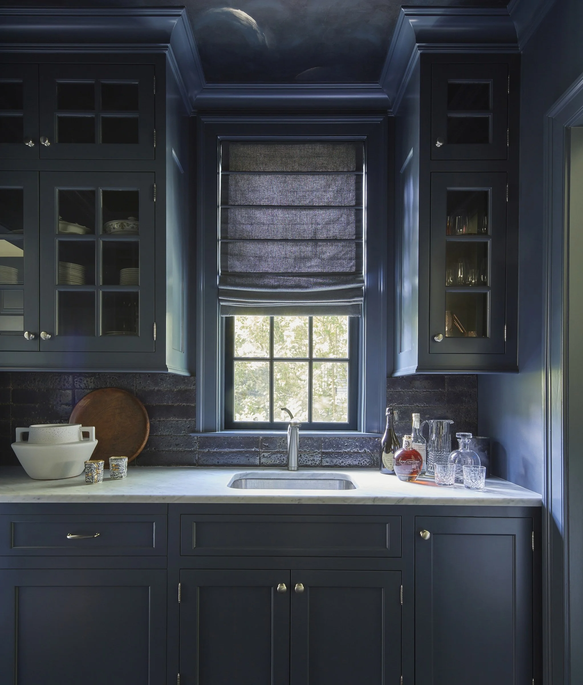 Dark blue pantry with glass-front cabinets and a window shade