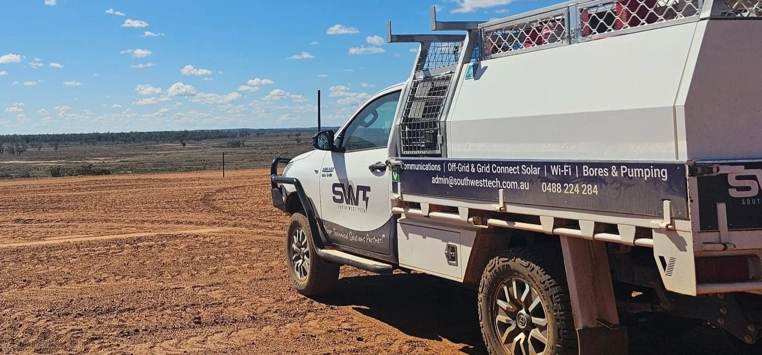 White utility truck with company logo and advertisement parked on a dirt field under a blue sky with clouds, distant trees on the horizon.