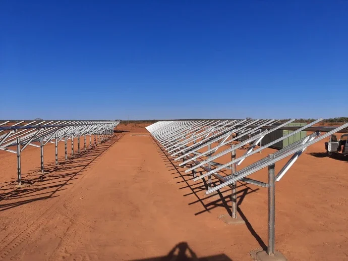 Solar panels installed on a dirt field under a clear blue sky.