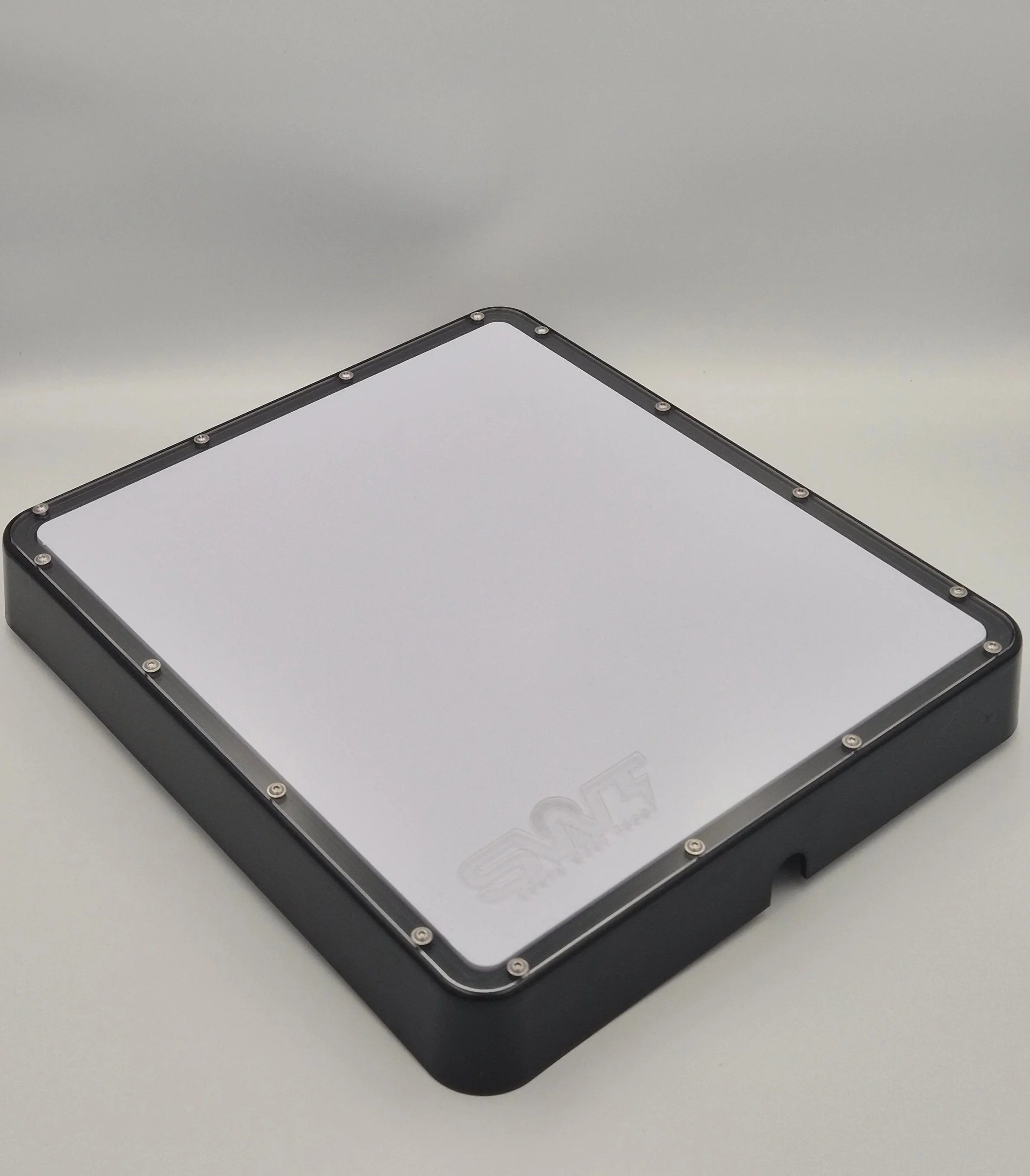 Close-up of a rectangular LED light panel with a white surface and black frame, secured with silver screws, placed on a gray surface.