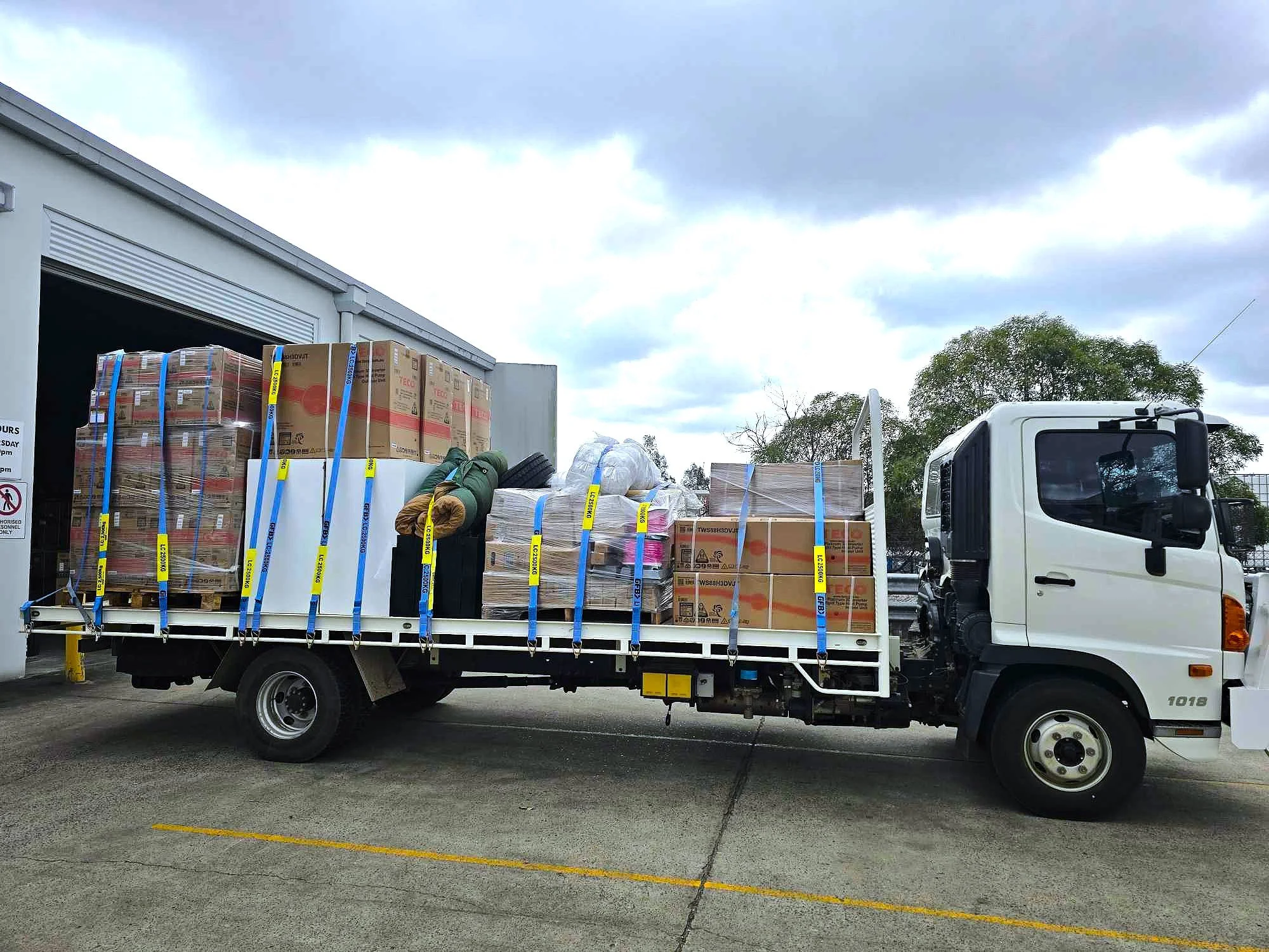 Pickup truck with a flatbed loaded with cardboard boxes, wrapped items, and supplies parked in a lot under cloudy sky.