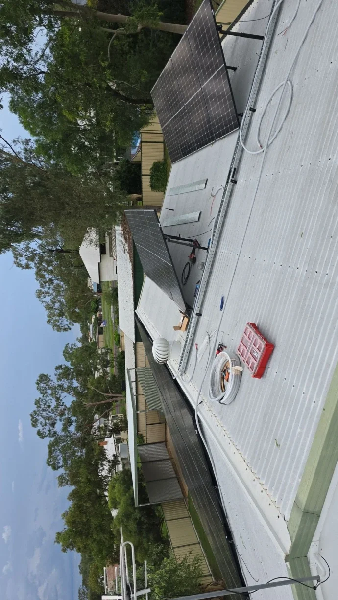 Solar panels installed on the roof of a building, with trees and neighboring houses in the background.