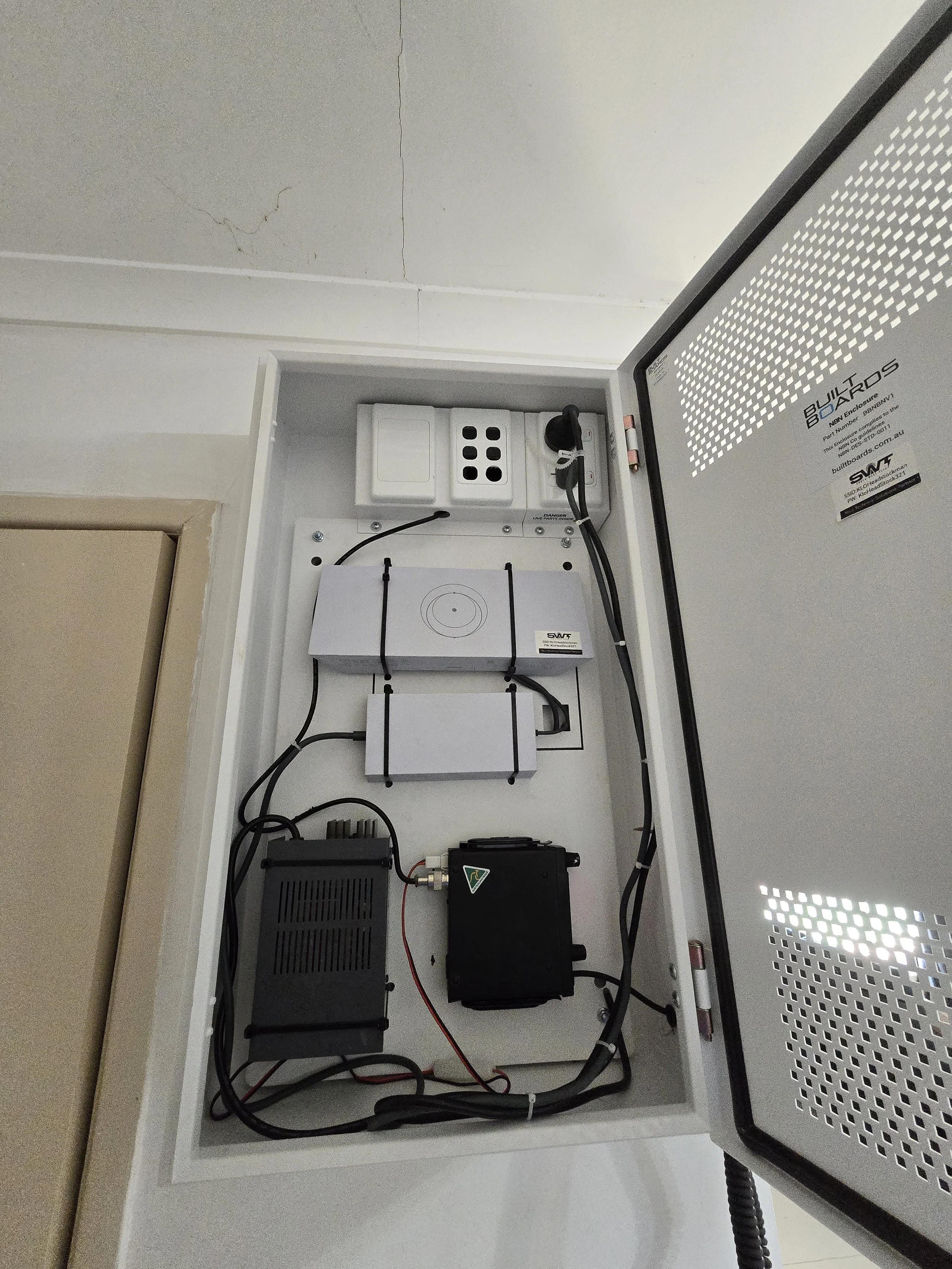 Electrical or electronic equipment setup inside a white box or cabinet with various components including a power strip, circuit boards, and cables, on a white surface.