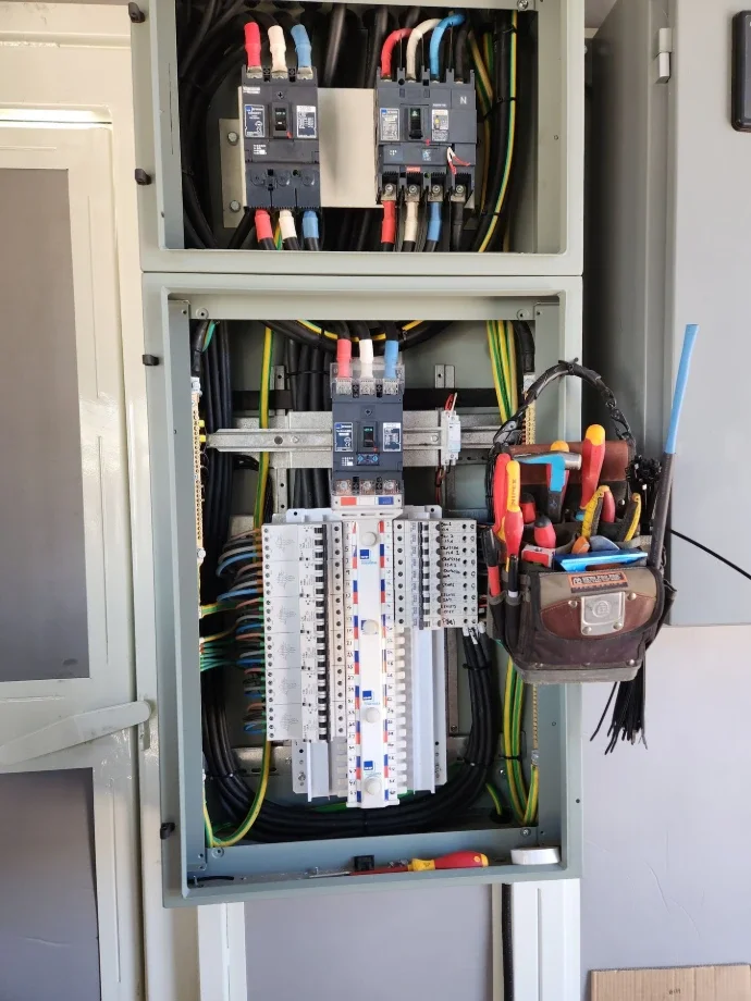 Electrical panel with circuit breakers and tools in a pouch attached to the side.