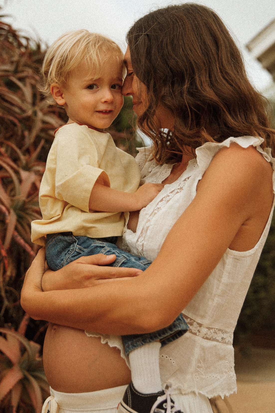 A woman holding a young boy close, both touching foreheads with their eyes closed, outdoors during sunset.